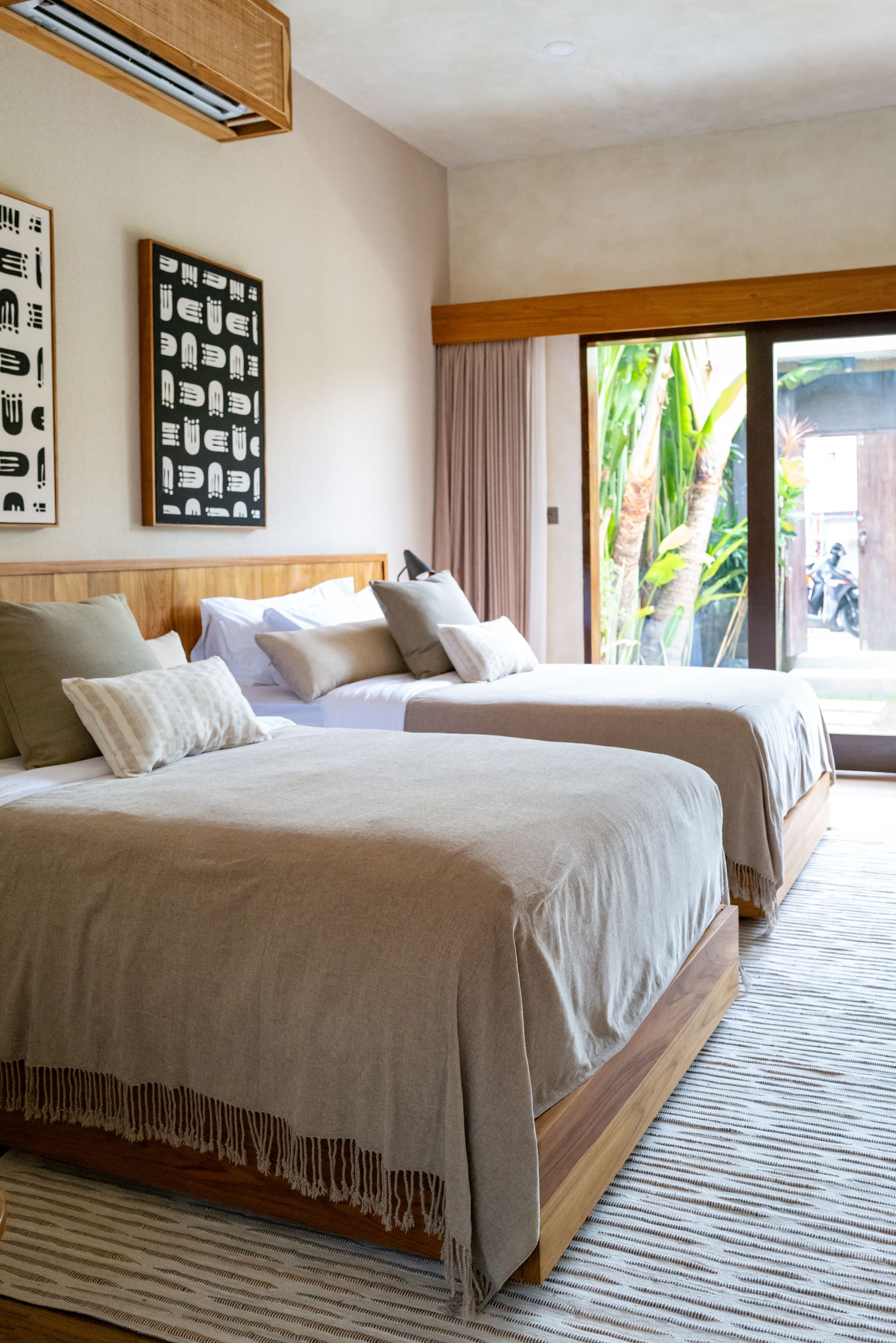 Two twin beds in a light-filled room with wood accents and a view of greenery.