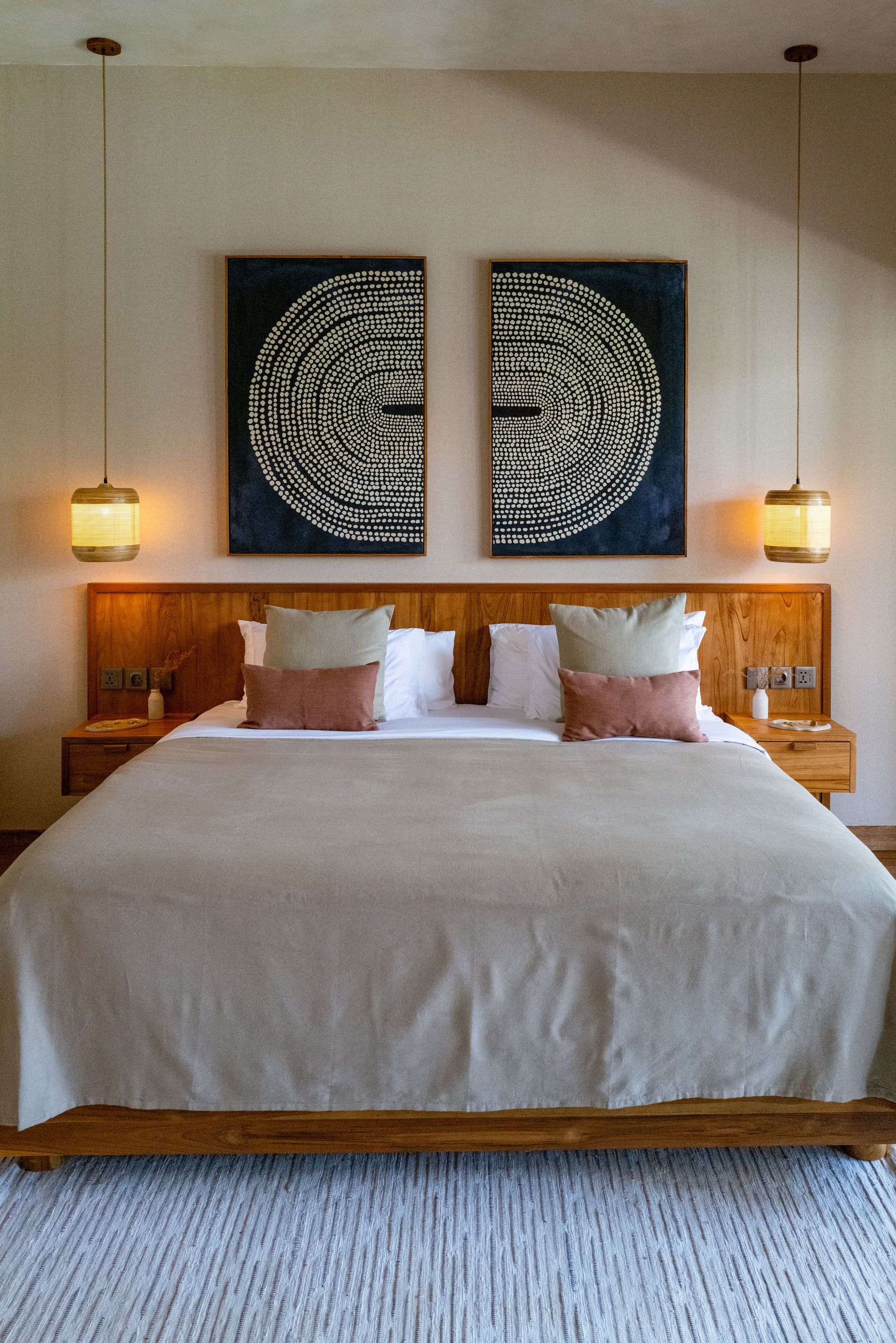 Bedroom with a wooden bed frame, two bedside tables, and two hanging lamps. Large artwork hangs above.