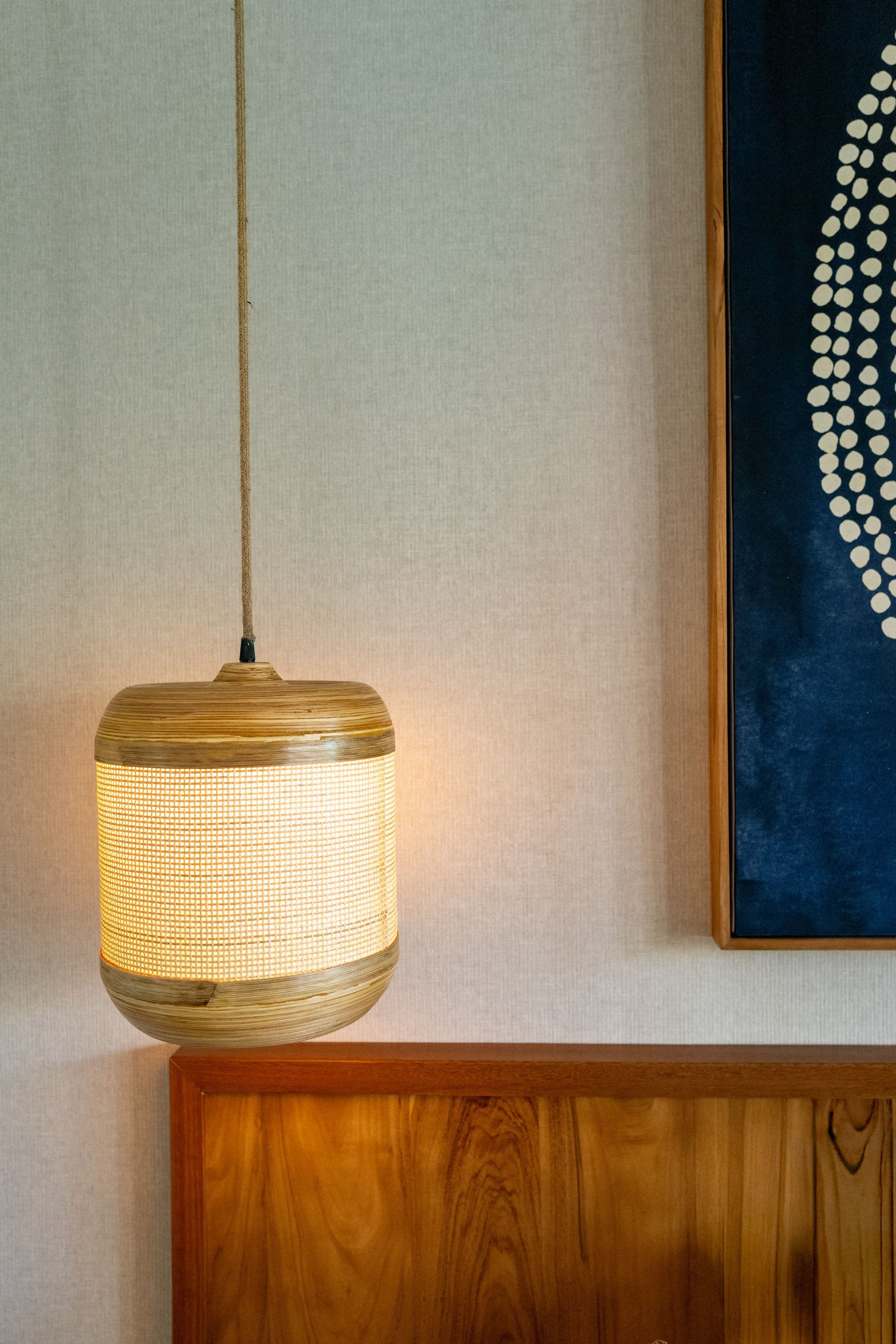 Woven pendant light fixture, hanging near a wooden headboard and a blue artwork.