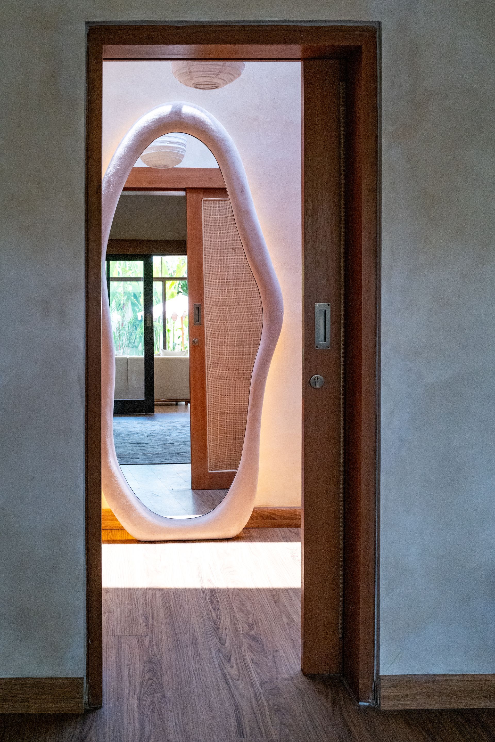 Wooden doorway frames an unusual, organic-shaped opening to another room. Light streams in; bamboo flooring.
