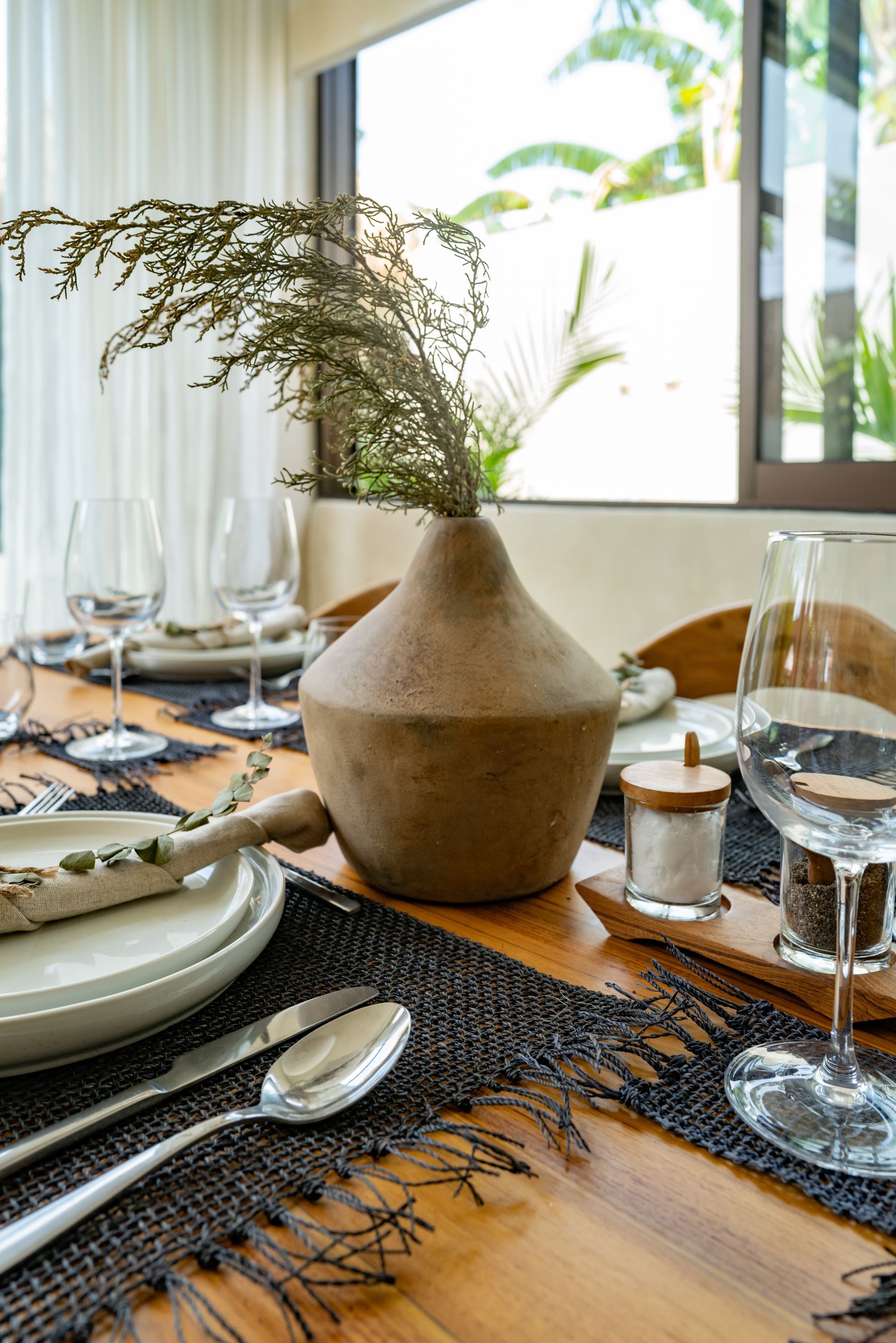 Dining table set with plates, silverware, glasses, vase of greenery, and salt shaker.