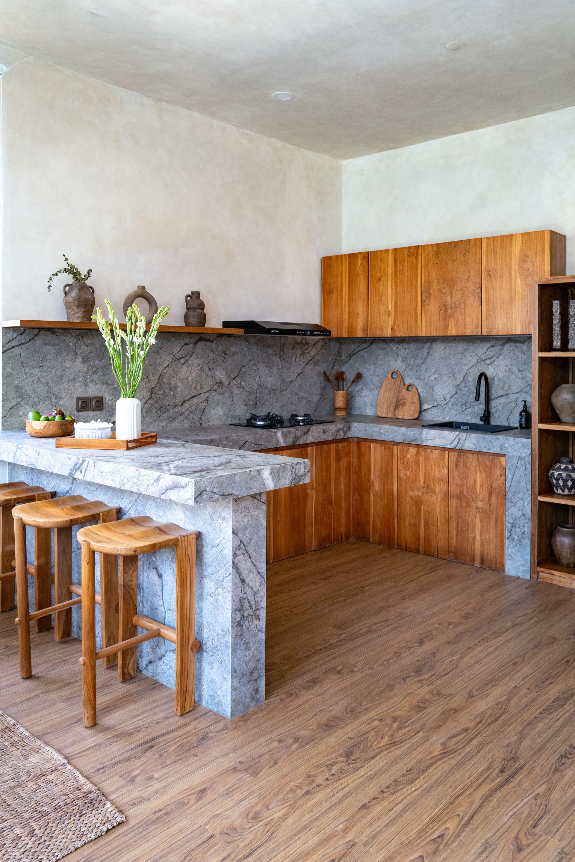 Wooden kitchen with stone island, wooden cabinets, and stools.