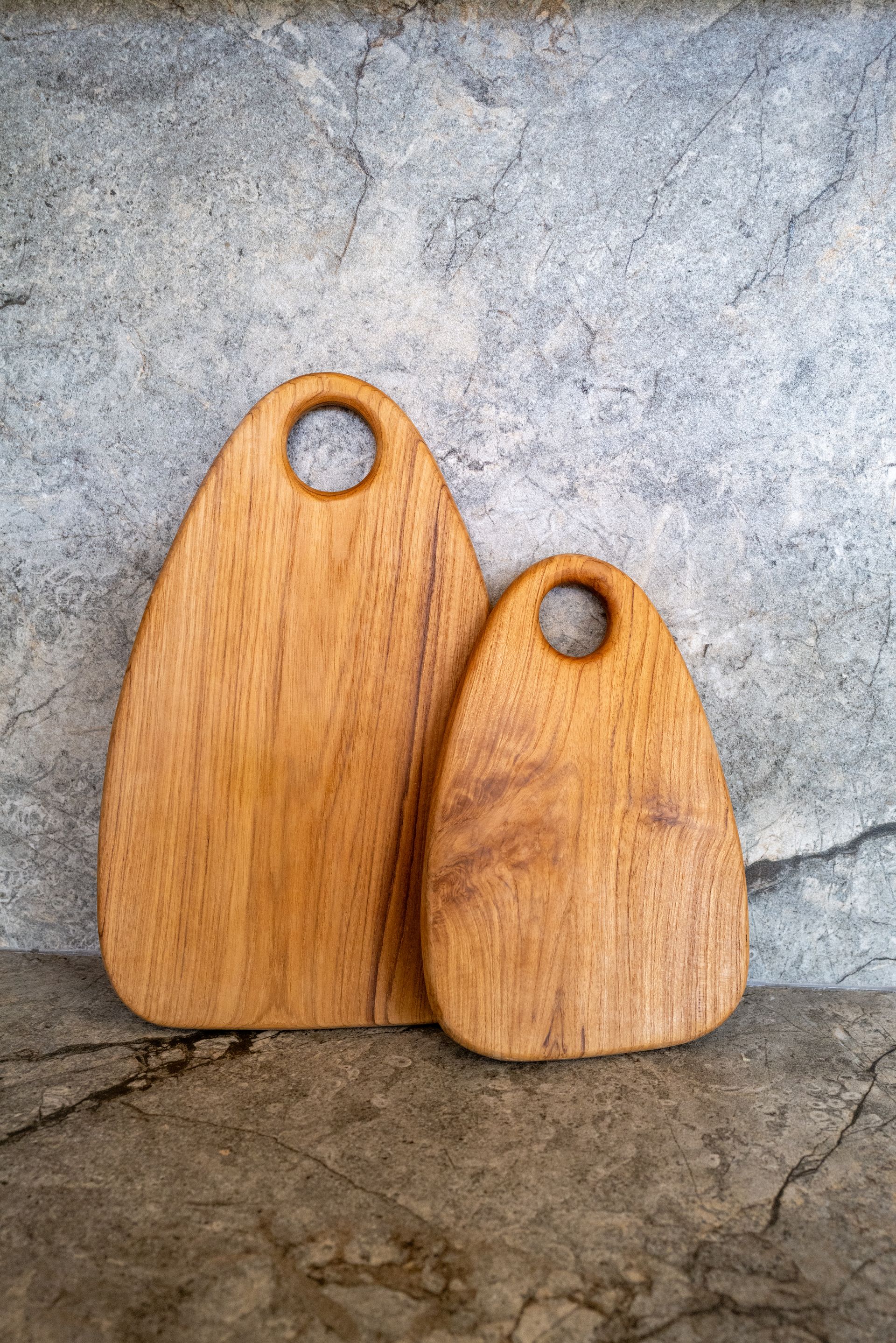 Two wooden cutting boards of different sizes with a handle hole, on a textured surface.