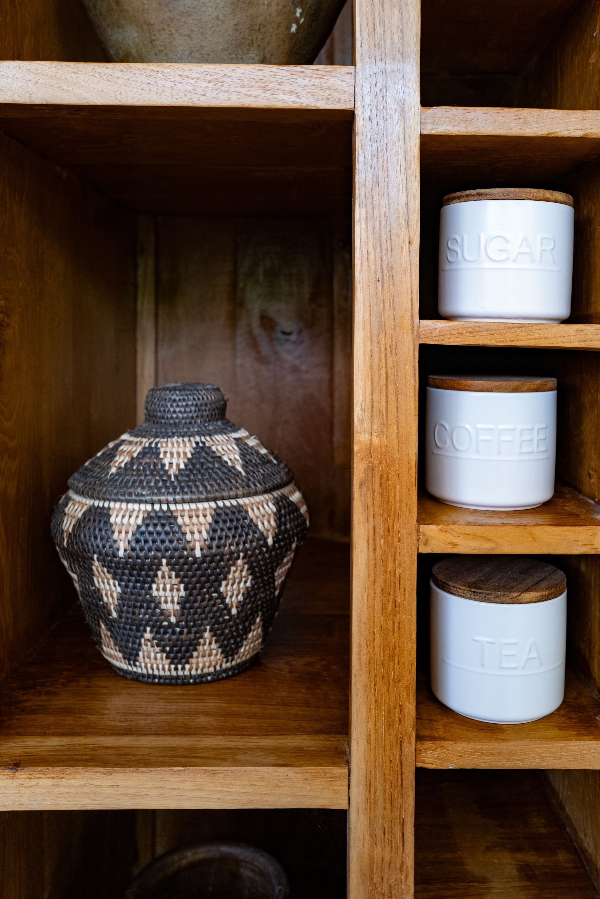 Wooden shelves with a decorative basket and white canisters labeled sugar, coffee, and tea.