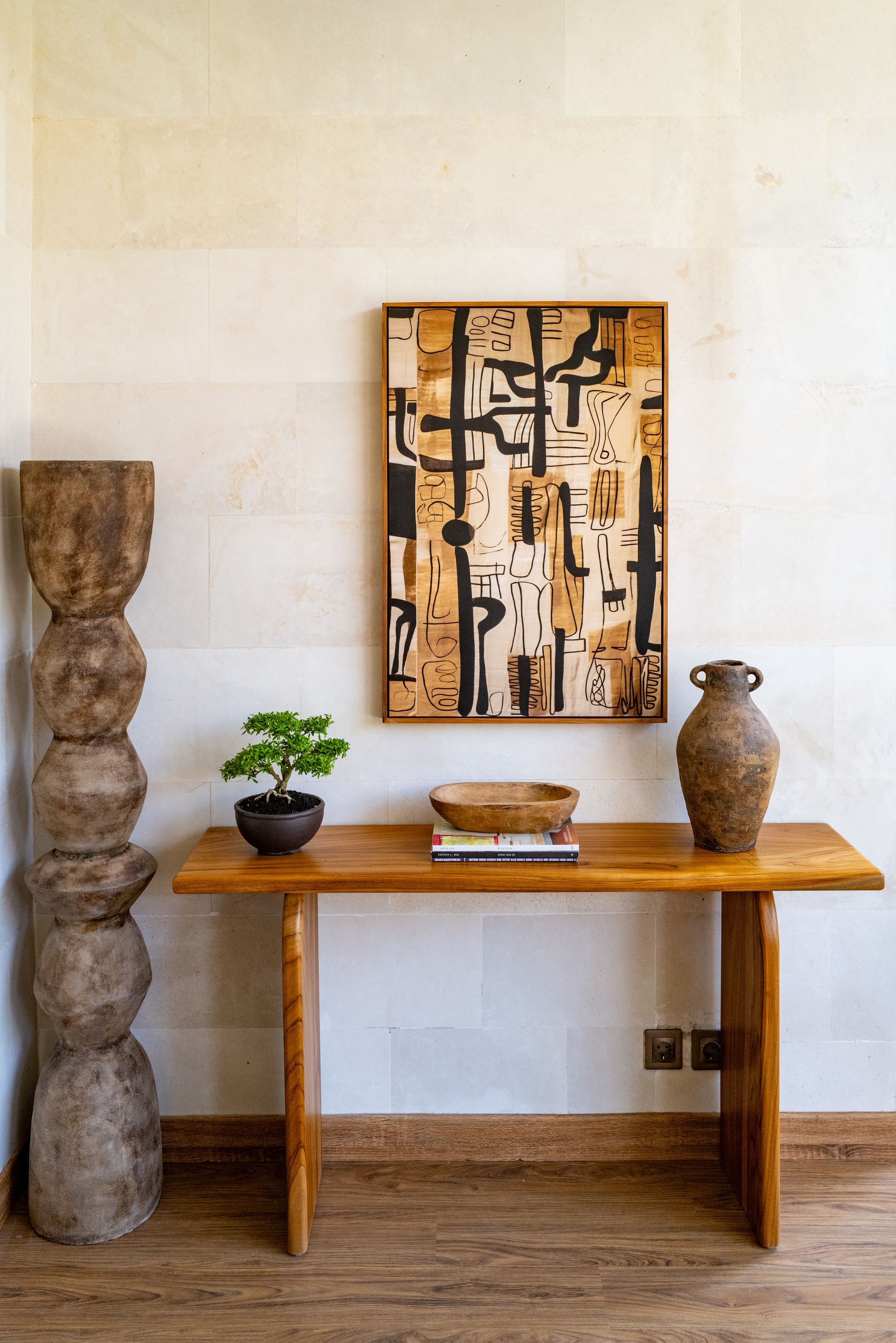Wooden console table with artwork, pottery, and sculpture against a textured wall.