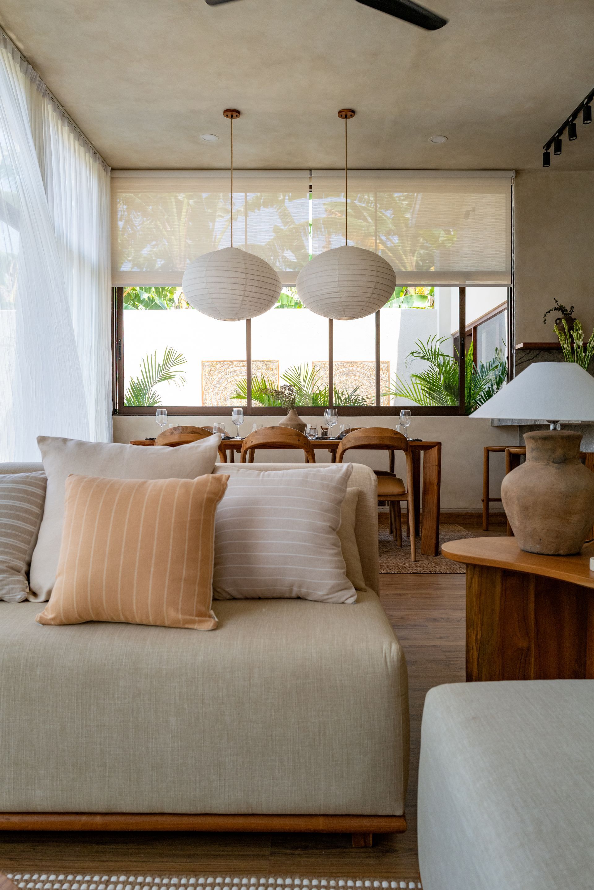 Living room with sofa, pillows, and paper pendant lights. Sunlight streams through a window.