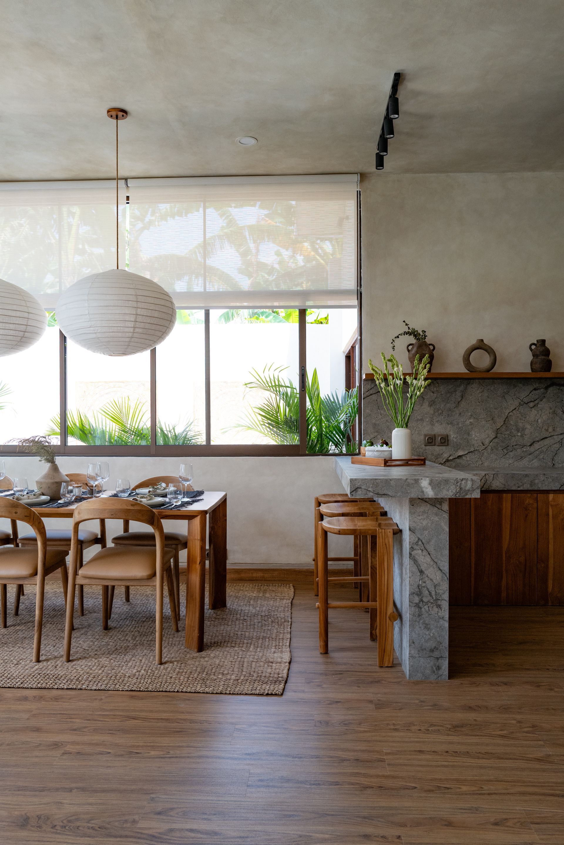 Dining room with wooden table, chairs, bar stools, and window overlooking greenery.