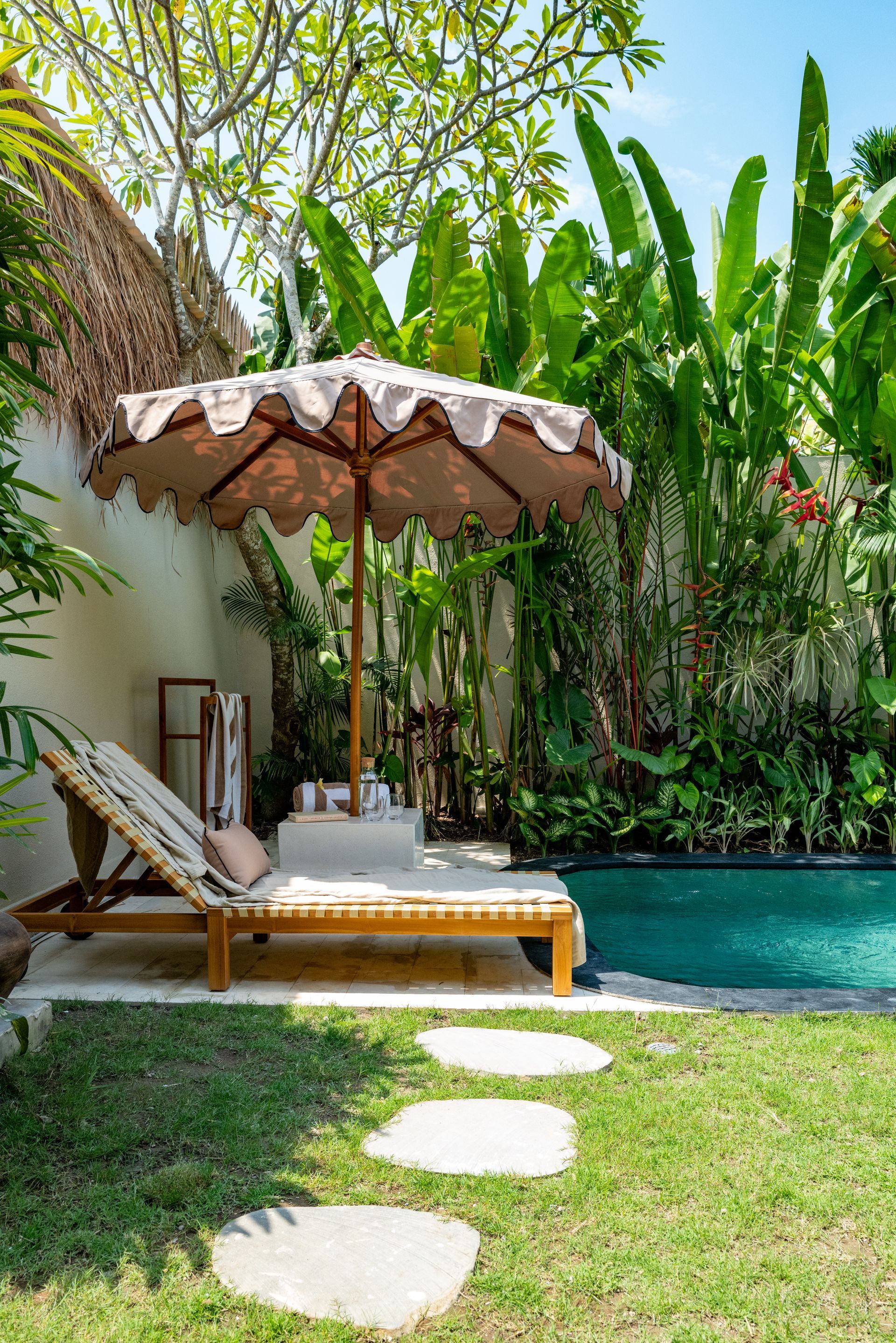 Lounge chair with umbrella by a pool in a tropical garden.