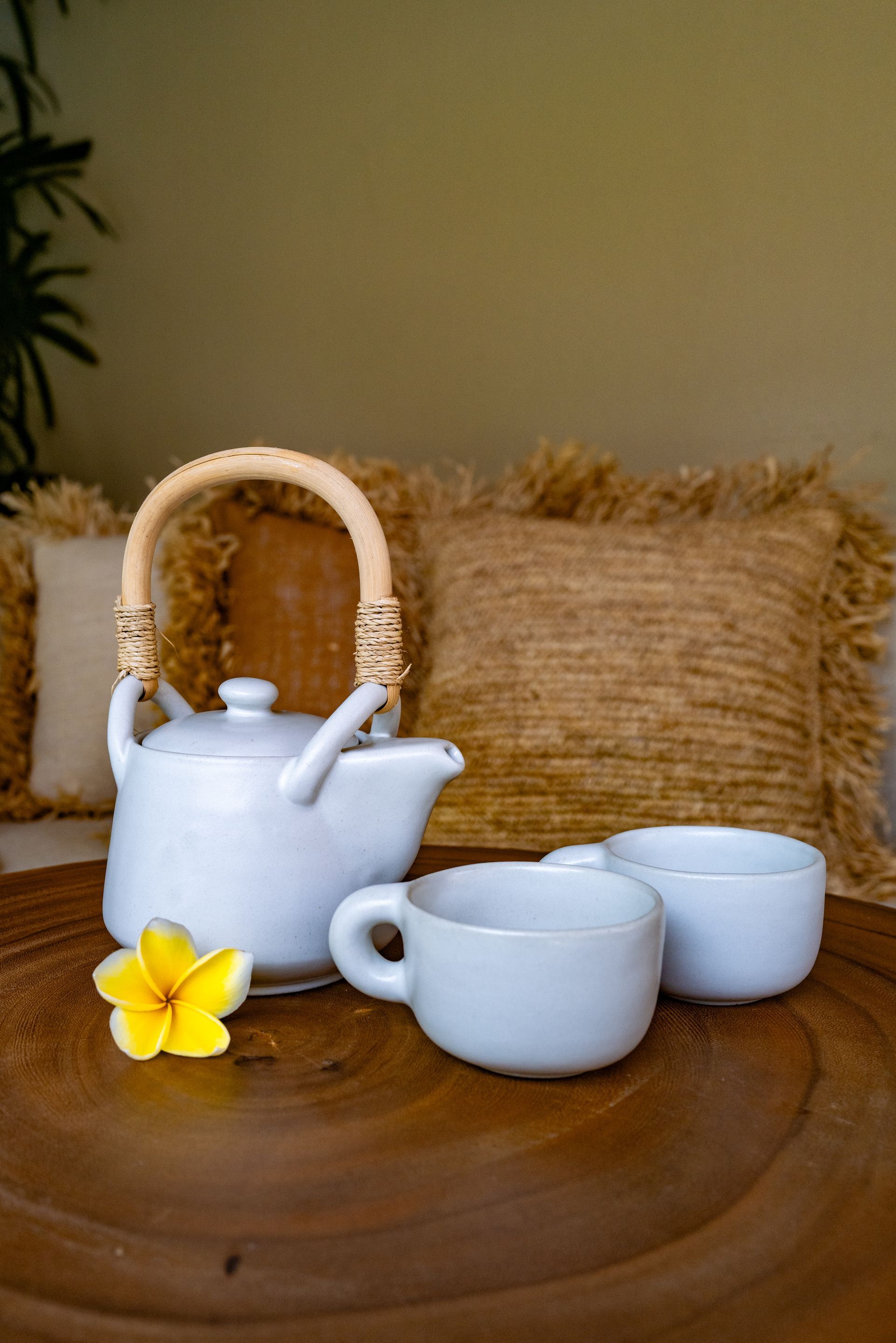 White teapot and cups on wooden table with yellow flower.