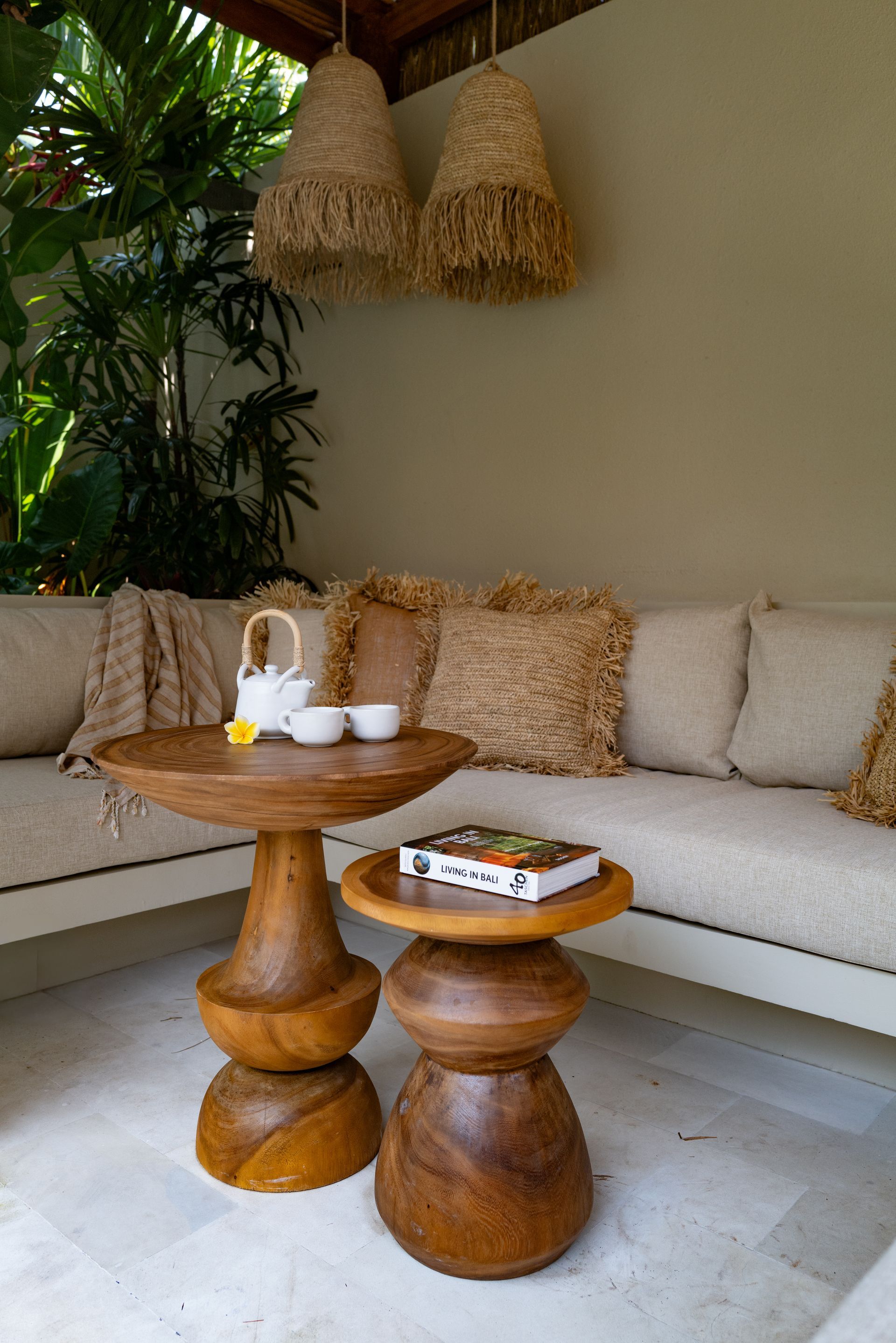 Outdoor seating area with beige couch, wooden tables, tea set, and woven pendant lights.