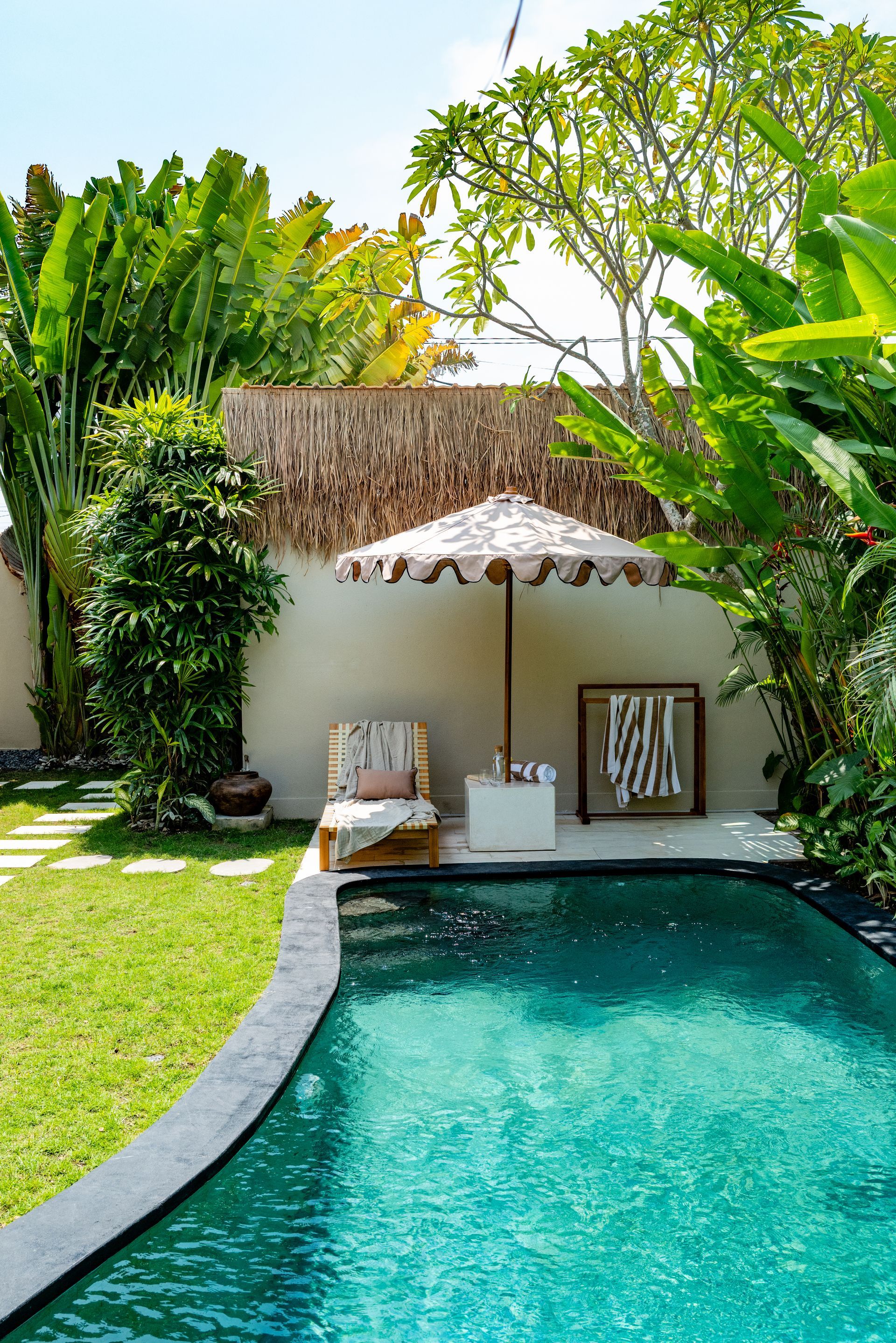 Swimming pool in a tropical garden with lounge chair under an umbrella.
