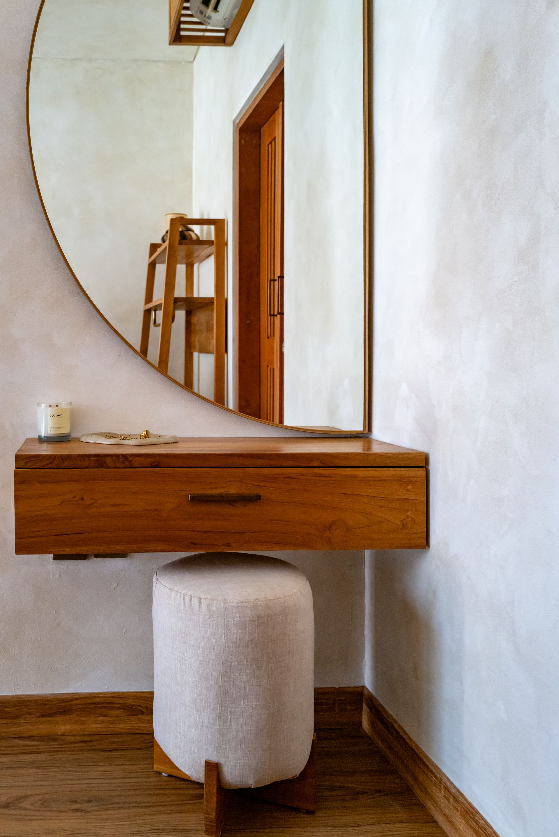 Wooden floating vanity with a round mirror, stool, and candle.