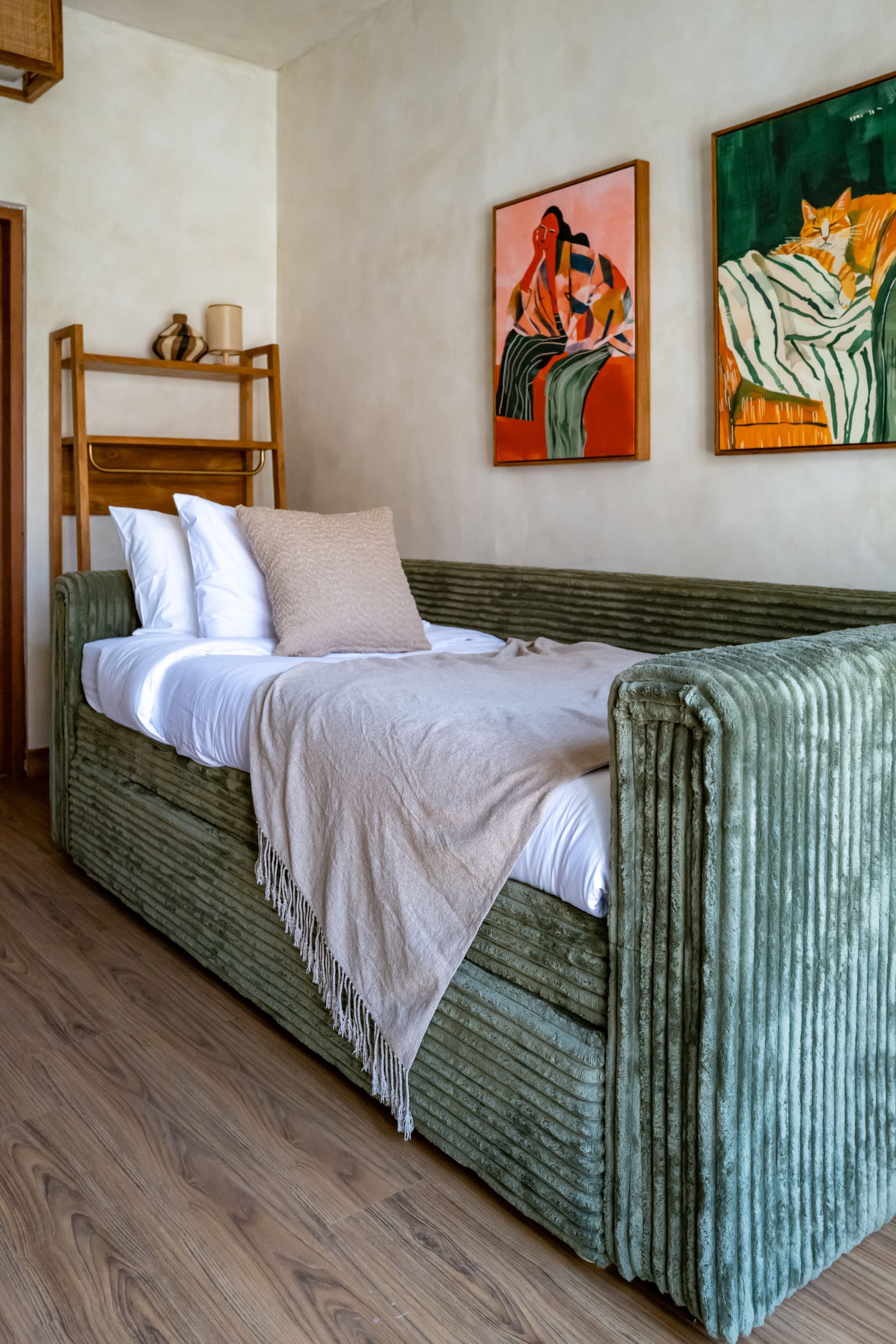 Green corduroy daybed in a room with art and wooden shelves.