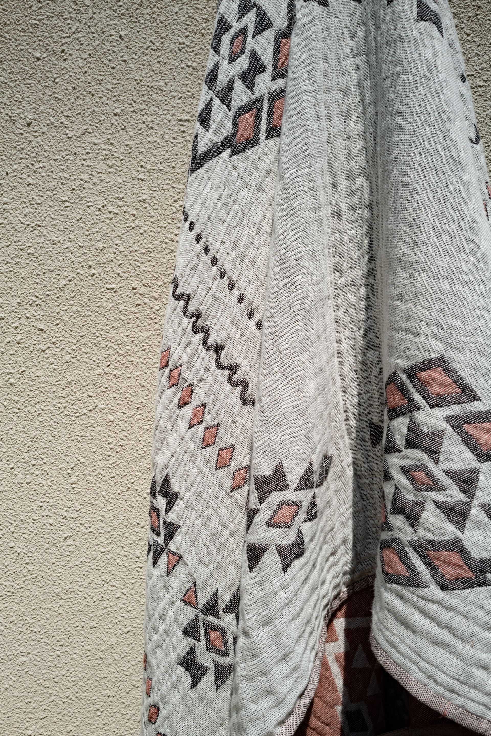 Gray and patterned cardigan draped against a stucco wall, featuring geometric designs in black and reddish-brown.