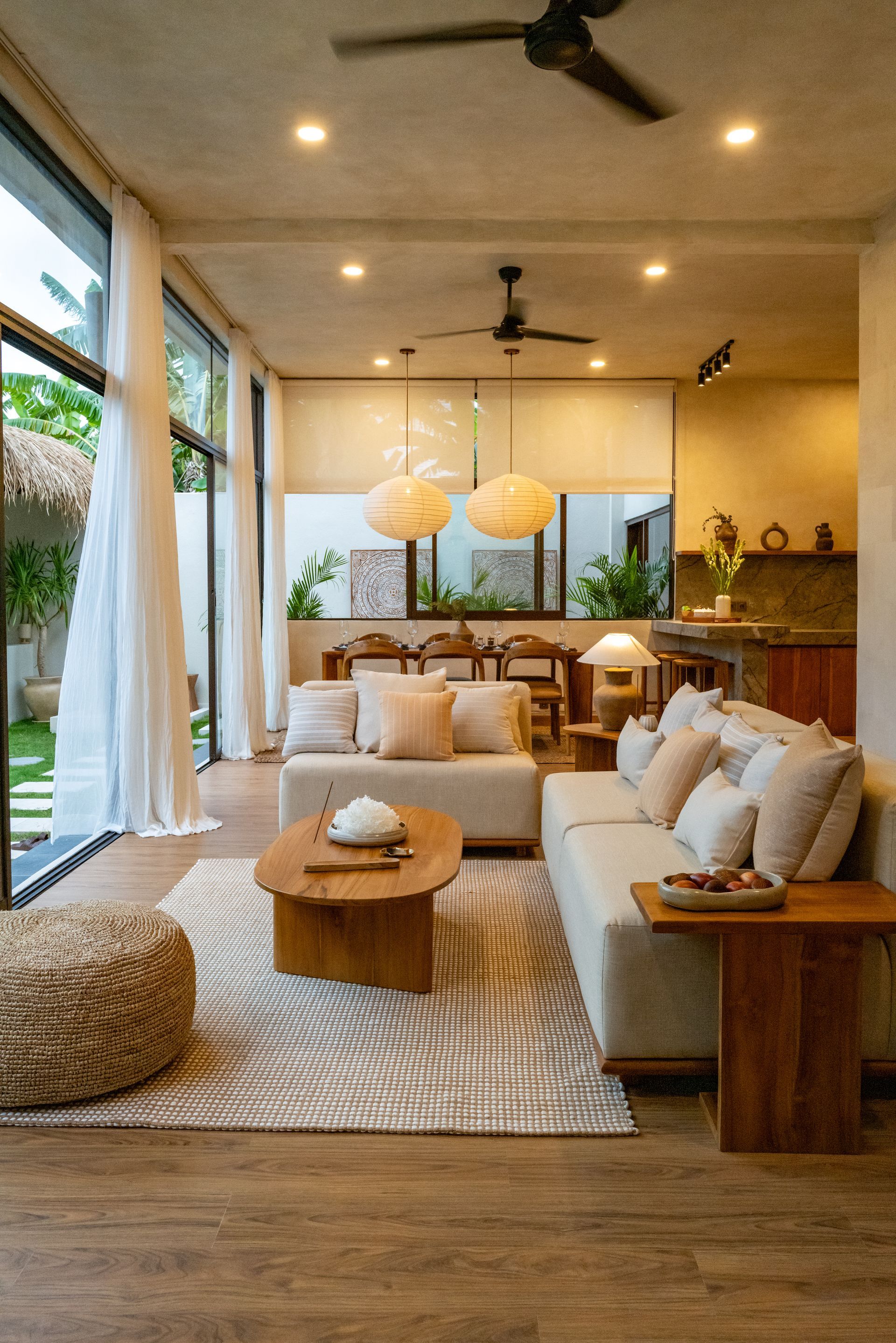 Living room with beige couches, wooden coffee table, large windows, and natural light.