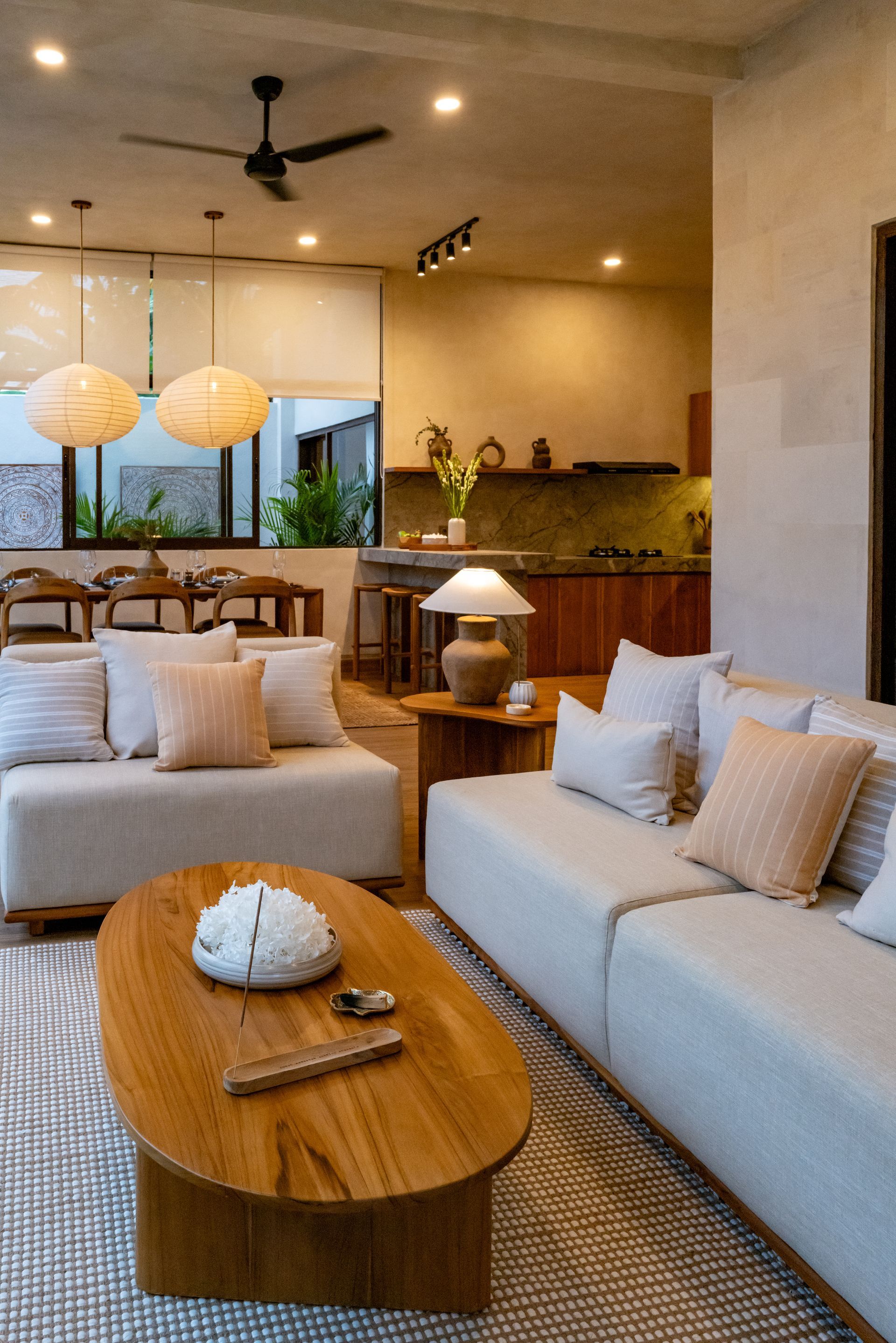 Cozy living room with light sofas, wooden coffee table, woven rug, and overhead lighting.