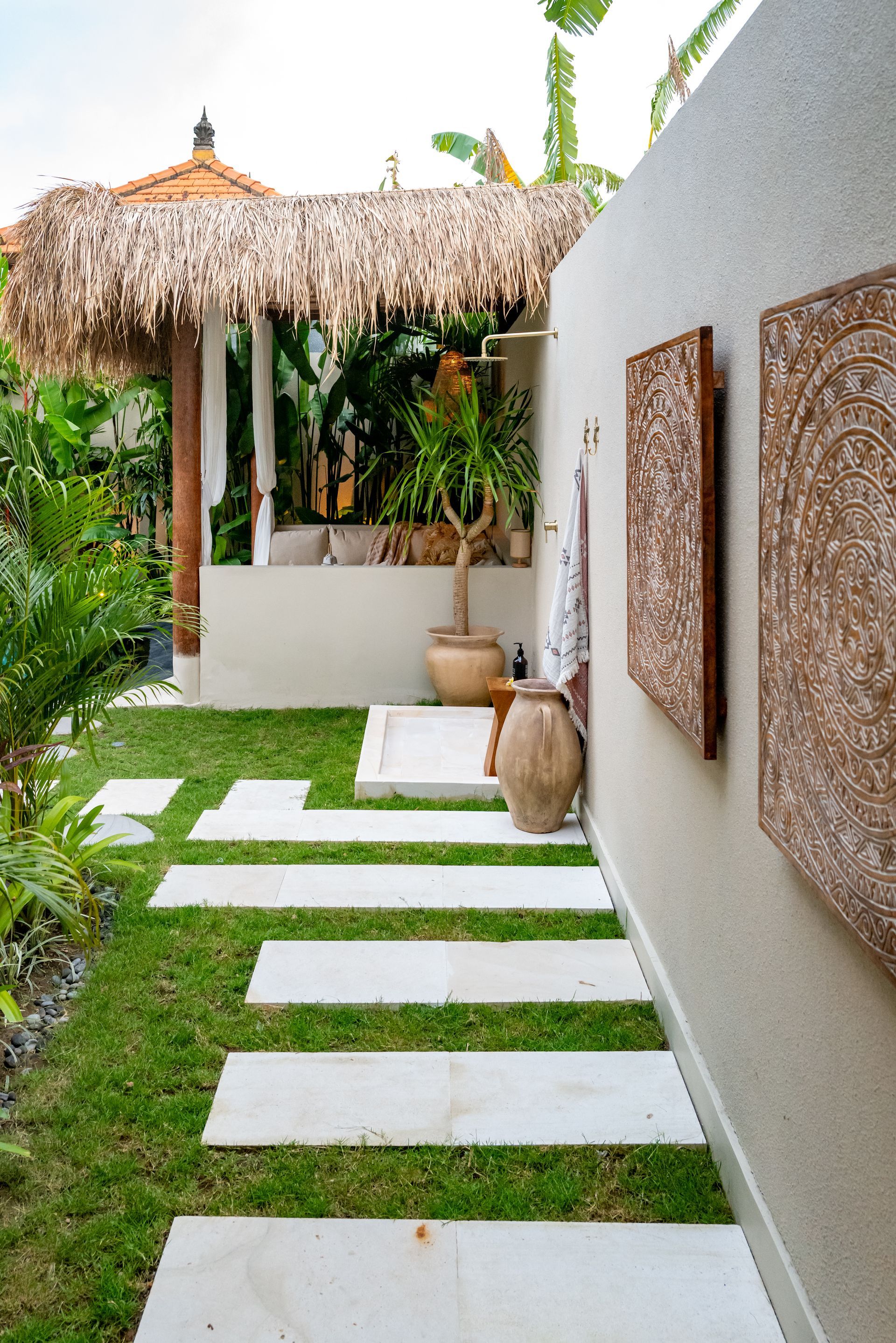 Pathway of white stone slabs through lush green lawn leads to a thatched roof gazebo.