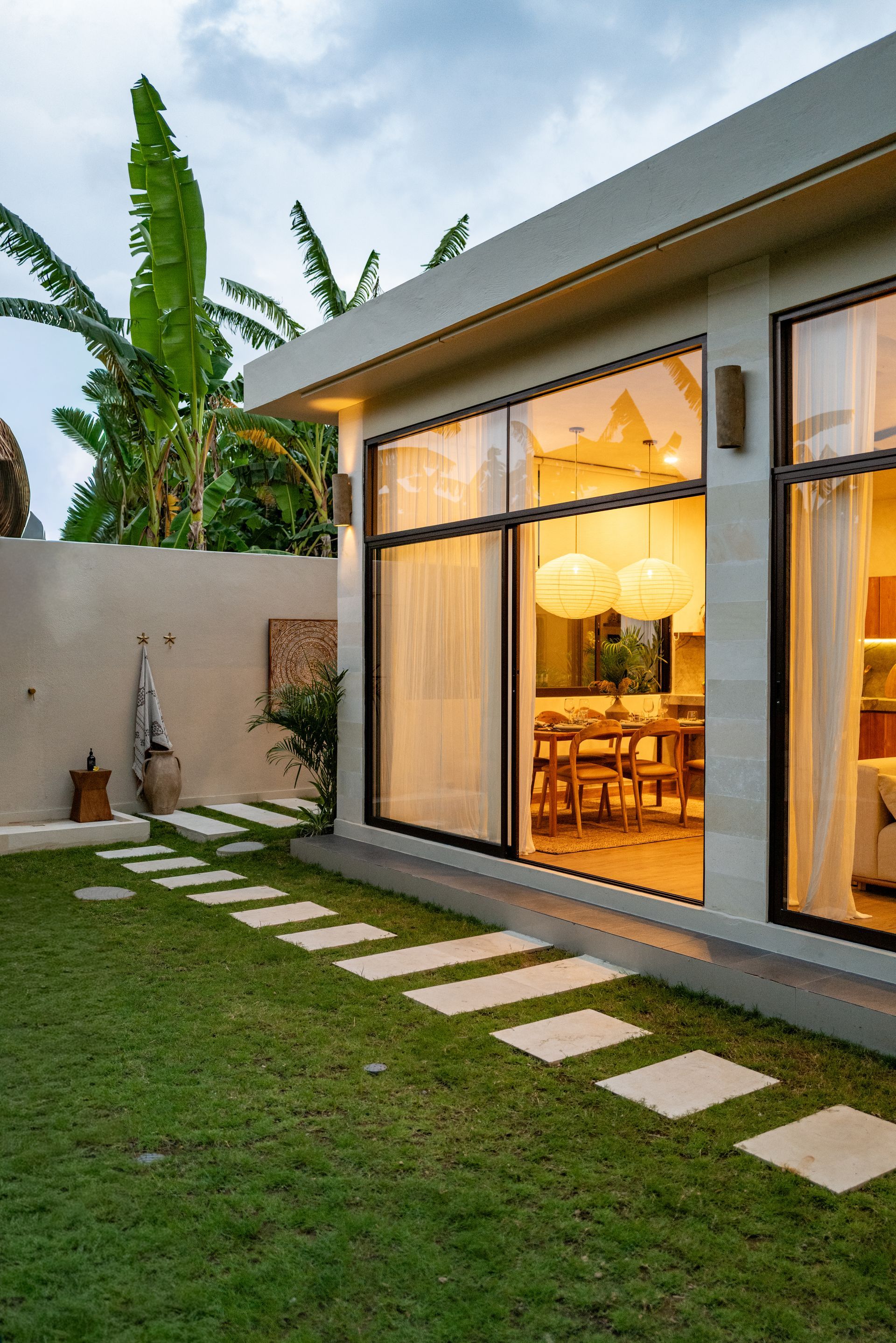 Exterior view of modern home with large windows, stone walkway, and lush green lawn.