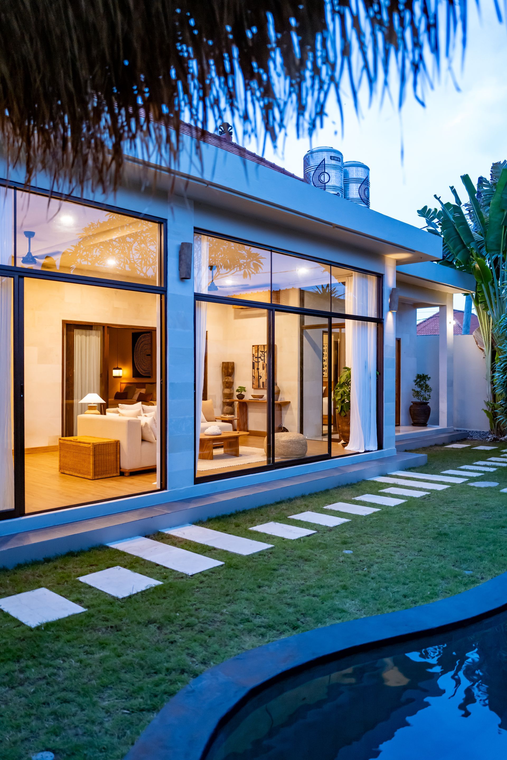 Modern house with large windows, grass yard, and a pool on a cloudy day.