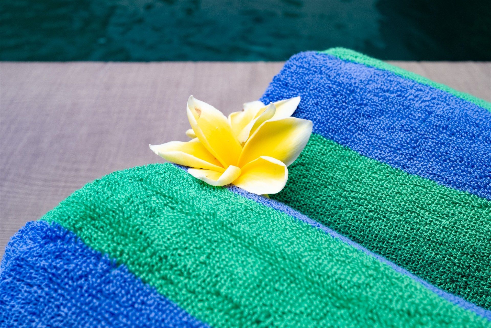 Rolled green and blue striped towels, yellow flower.