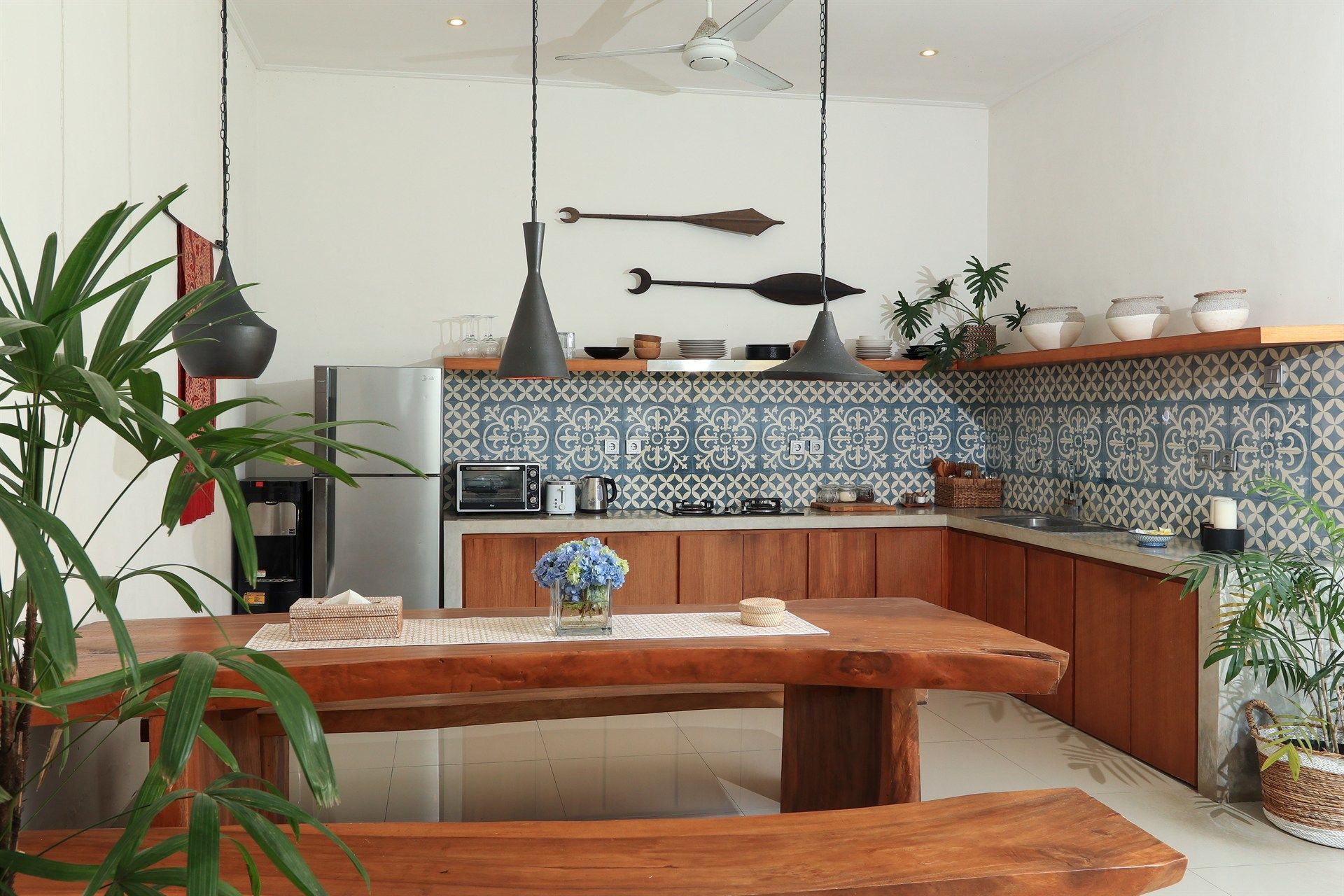 Kitchen with wood cabinets, blue tile backsplash, wooden table, and leafy plants.
