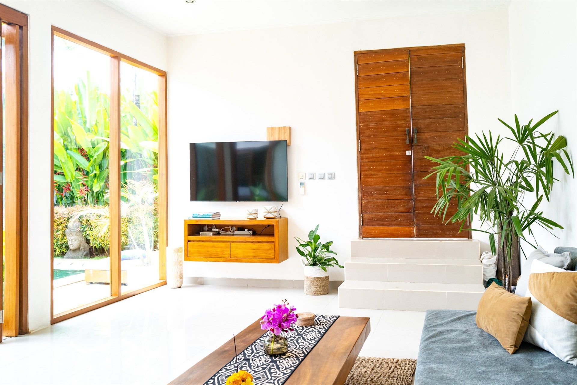 Living room with a large wooden door, TV, and sliding glass doors with a view of greenery.