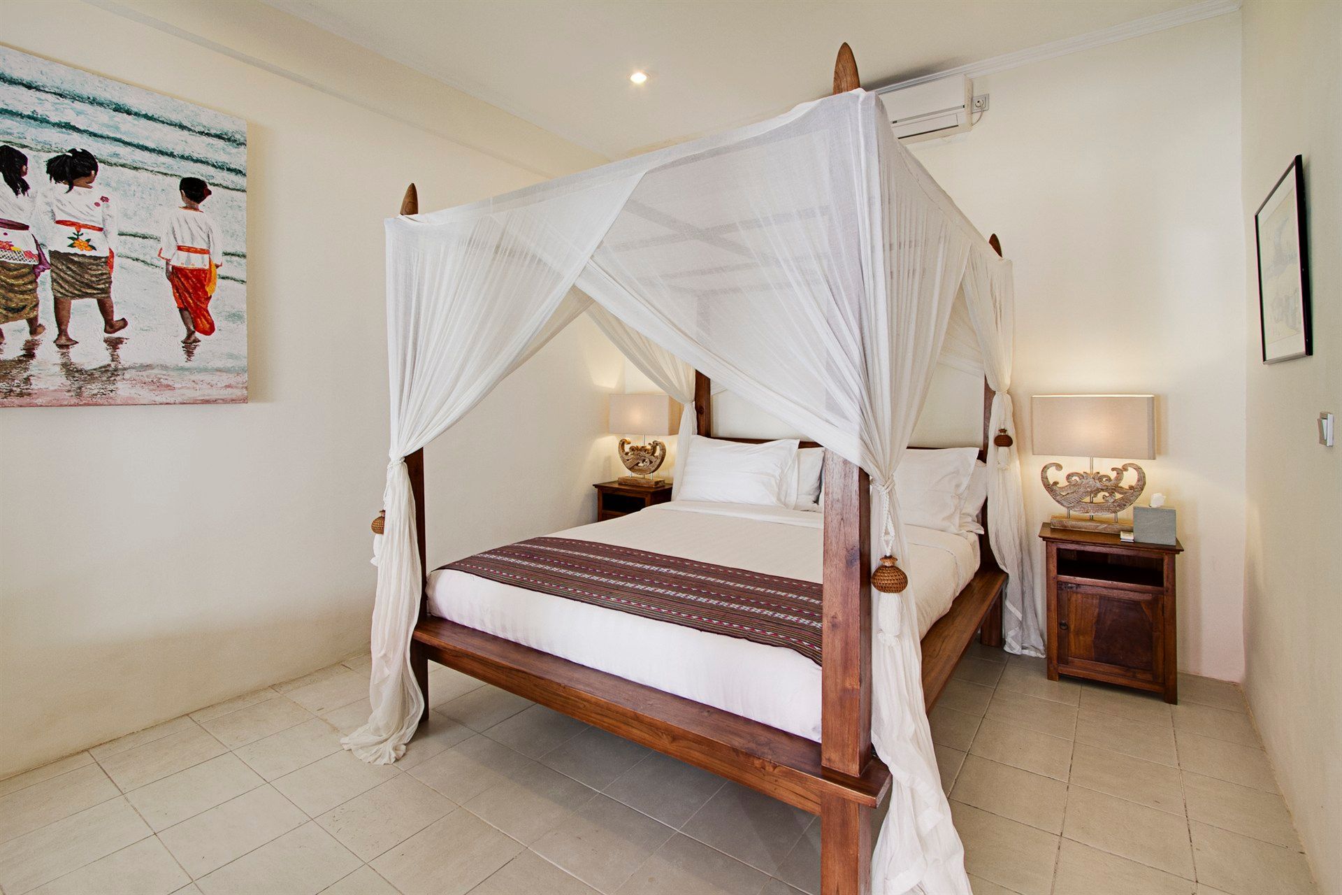 Bedroom with canopy bed, white bedding, nightstands, and artwork on a light-colored tile floor.