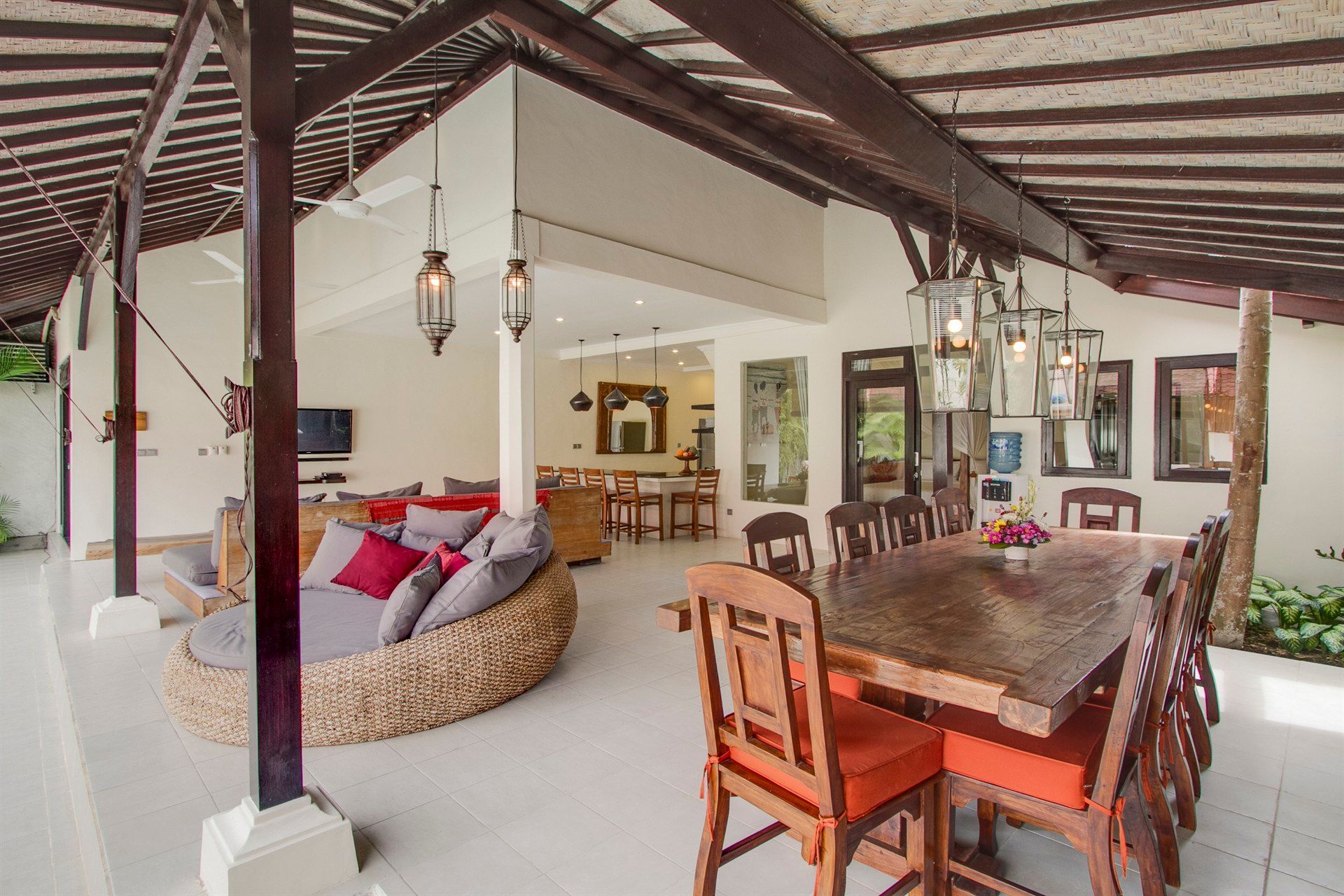 Open-air dining and lounge area. Wicker seating, wooden table, and hanging lanterns under a covered patio.