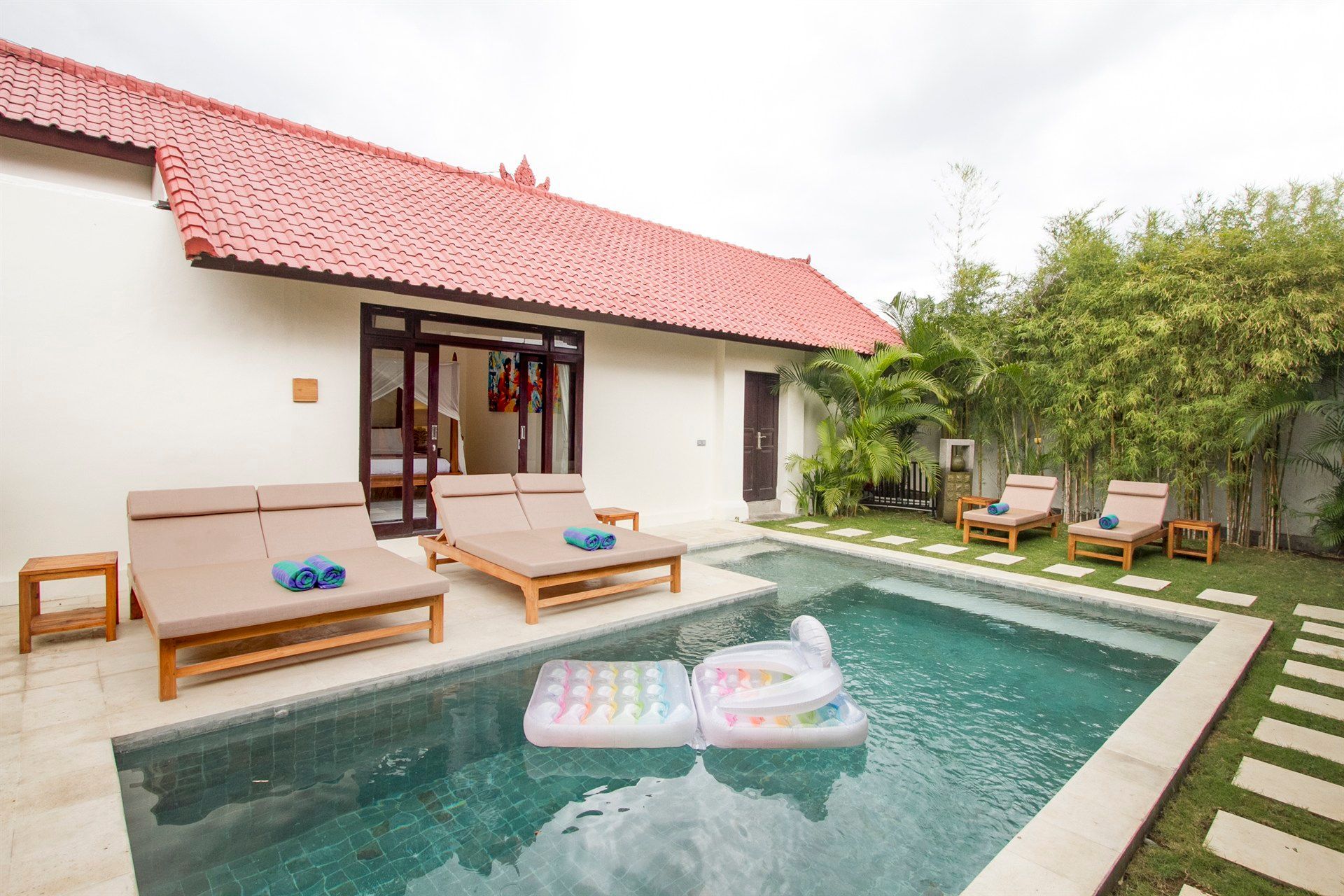 A large swimming pool in front of a white house with a red roof.