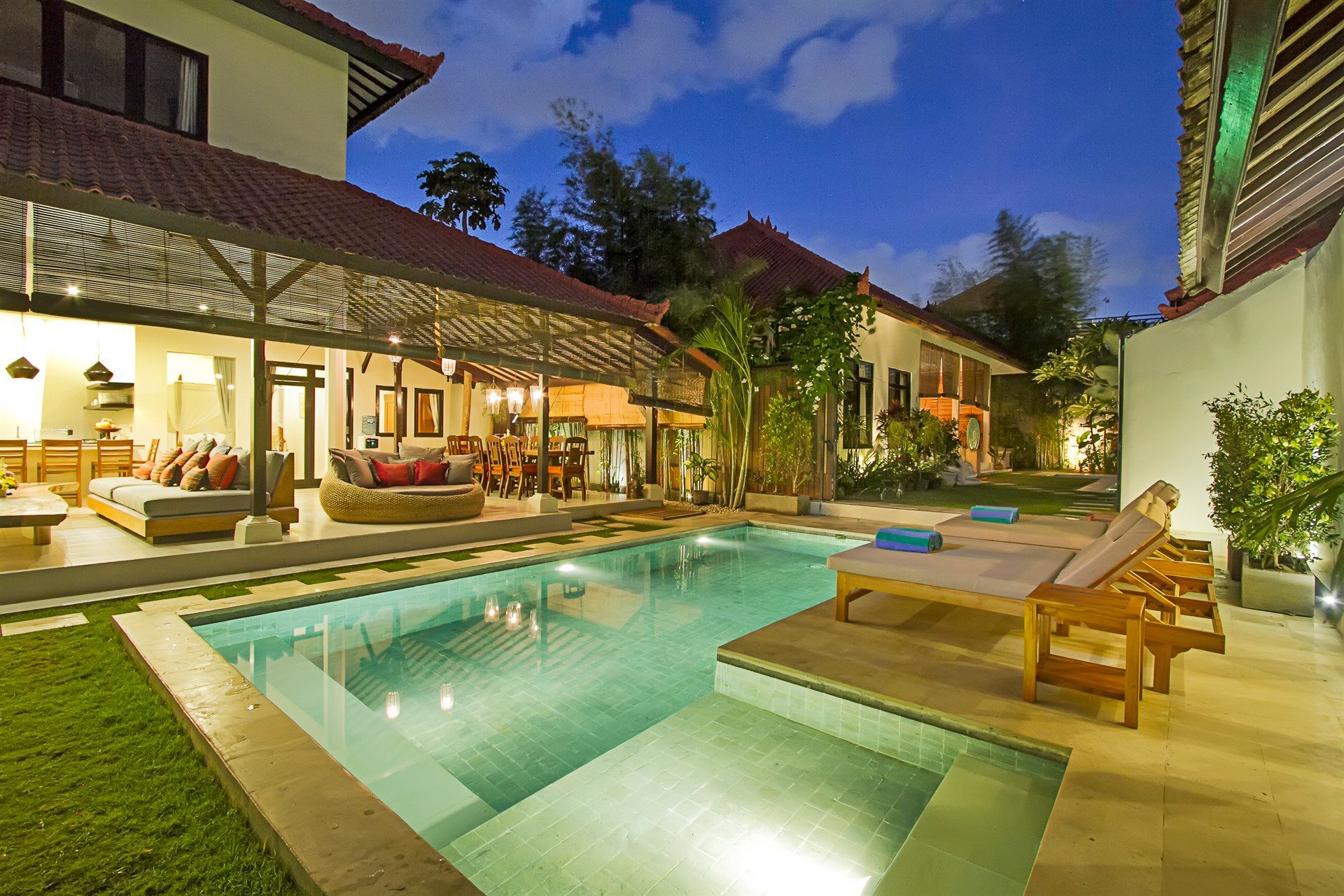 Villa with pool at dusk; open-air living area, lounge chairs, and tropical foliage.
