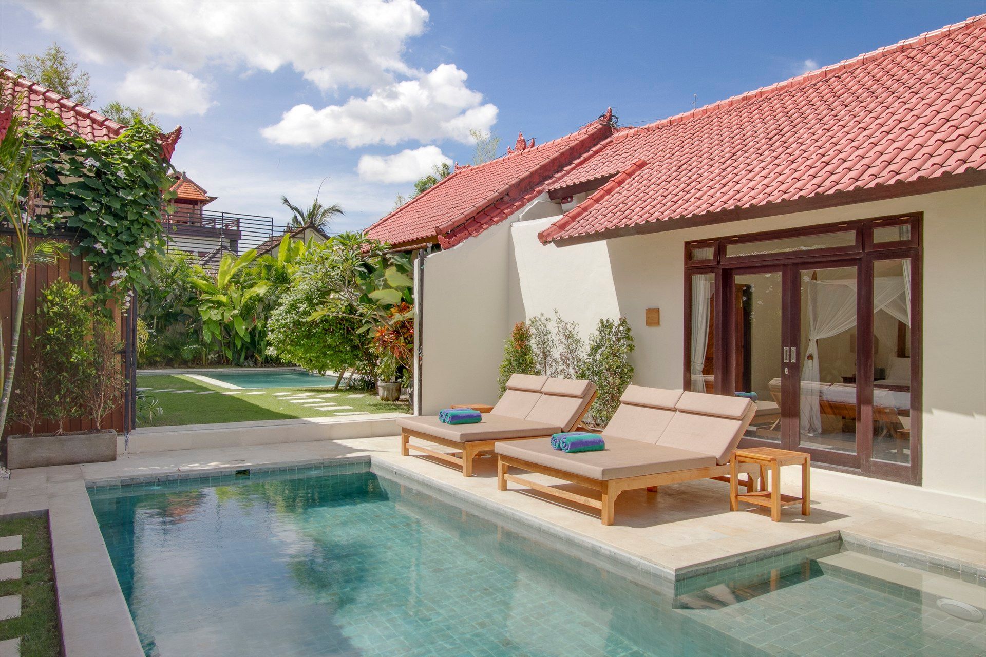 Swimming pool with lounge chairs in front of a white building with red tile roof, Bali, Indonesia.