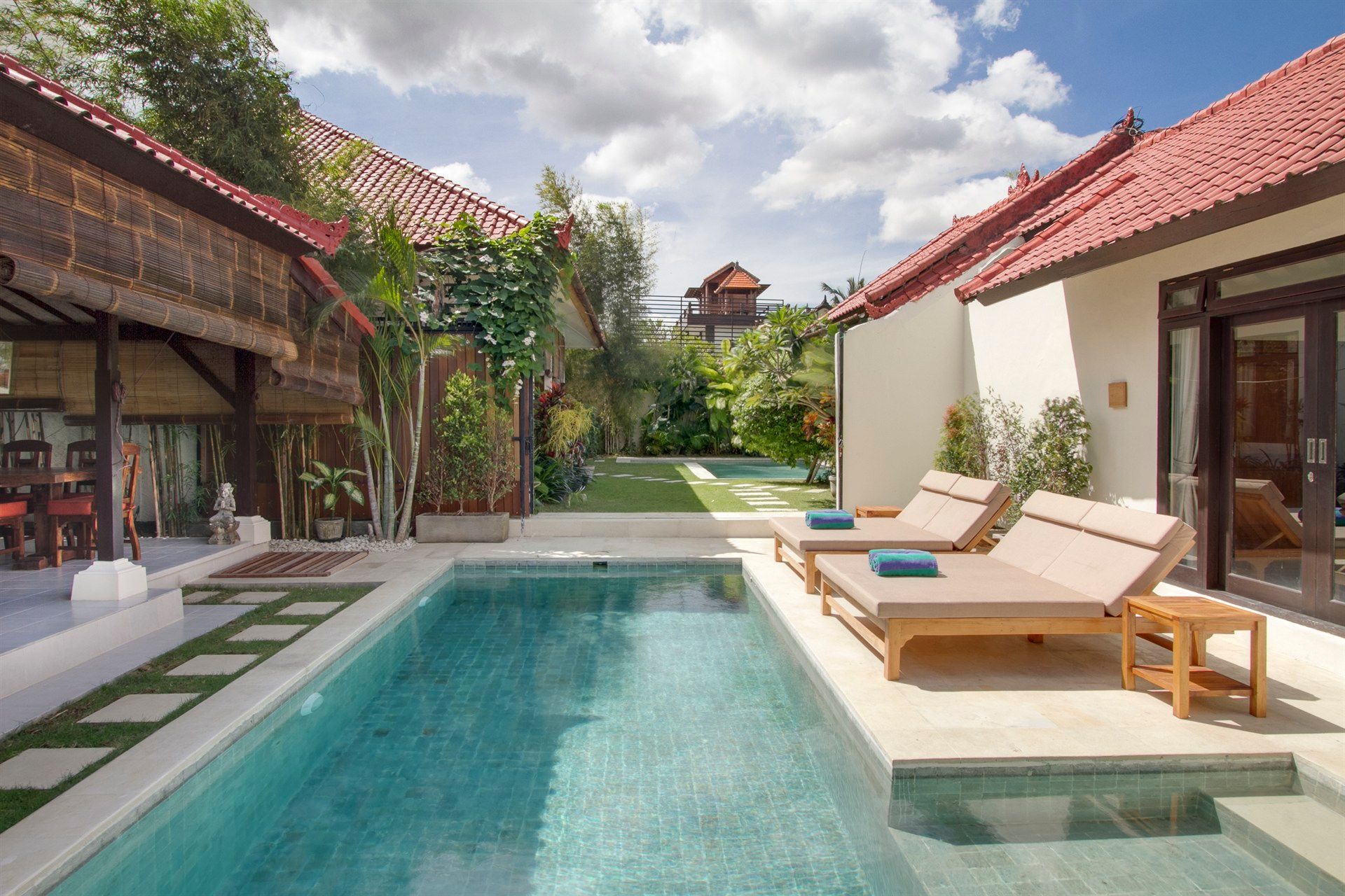 Pool and lounge chairs between two buildings with red tile roofs and a sunny sky.