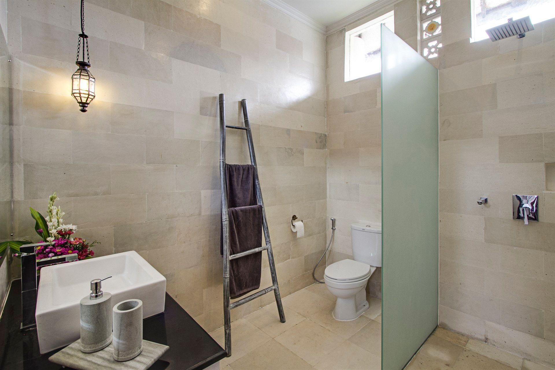 Modern bathroom with tan tile, white sink, ladder towel rack, and glass shower enclosure.