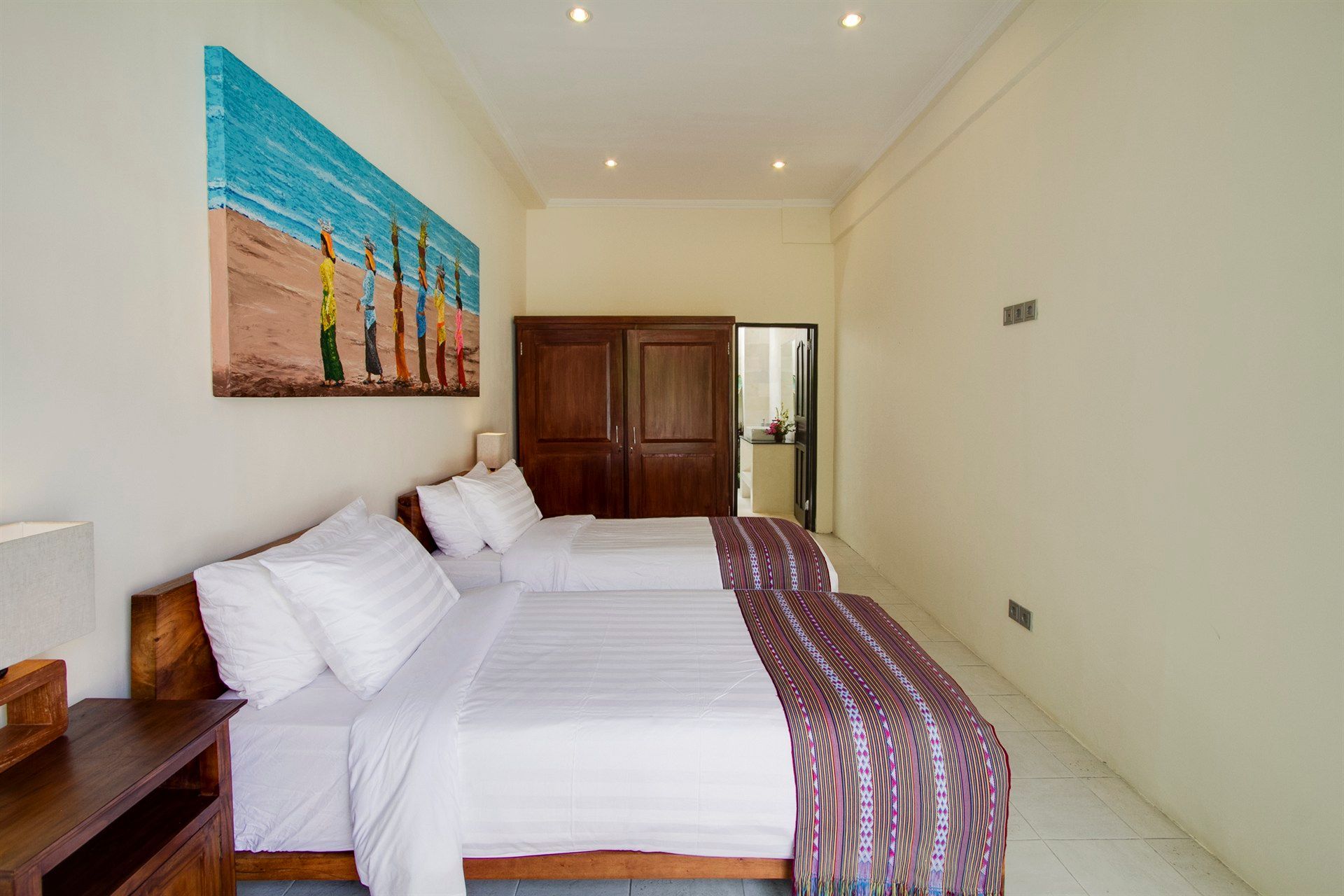 Bedroom with two beds, wooden furniture, and a painting of figures on a beach.