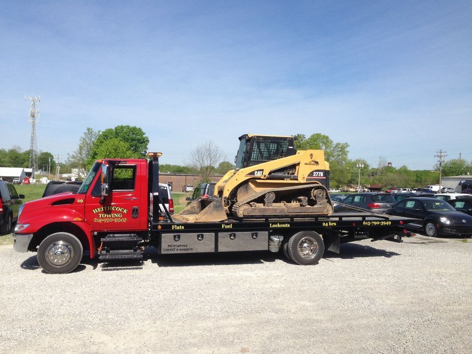 Red tow truck transporting a yellow Caterpillar skid steer loader on a sunny day.