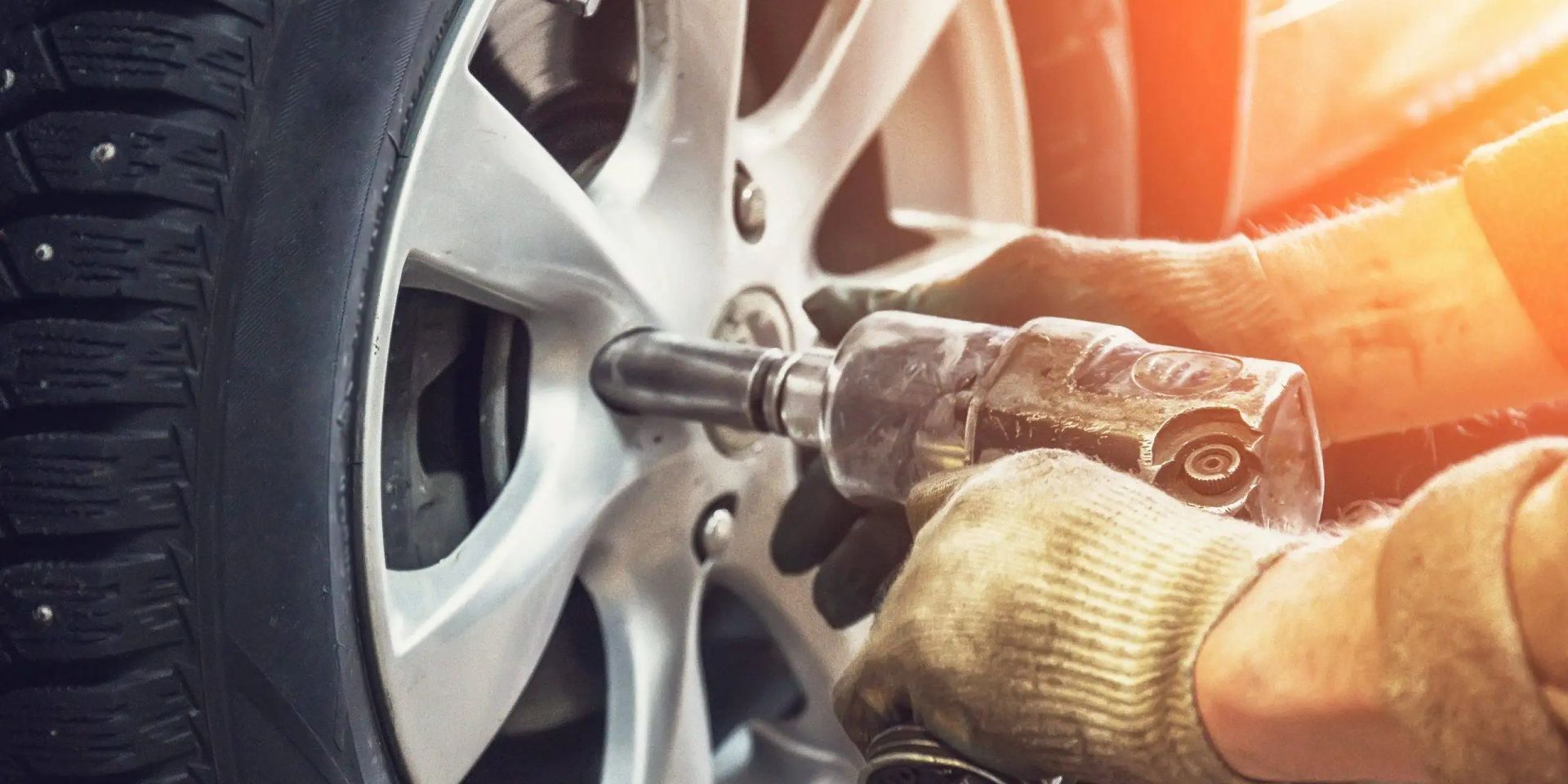 Hands wearing gloves using a tool to remove a car wheel bolt.