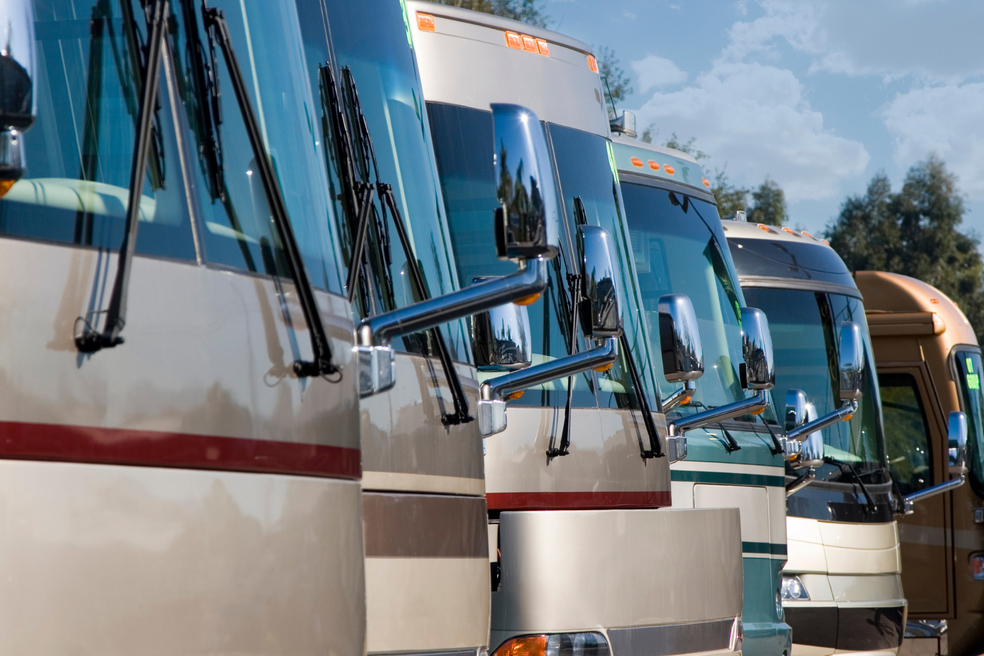 A row of large, modern recreational vehicles parked side-by-side in an outdoor lot.