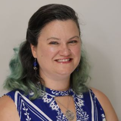Woman with dark hair and turquoise tips, smiling, wearing a blue and white patterned top.