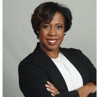 Woman in a black blazer smiles, arms crossed, pearl necklace.