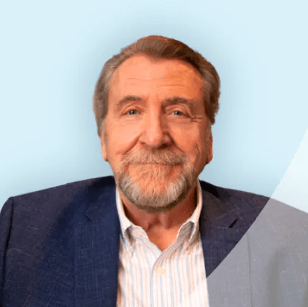 Man with a beard in a blue blazer smiles at the camera against a blue background.