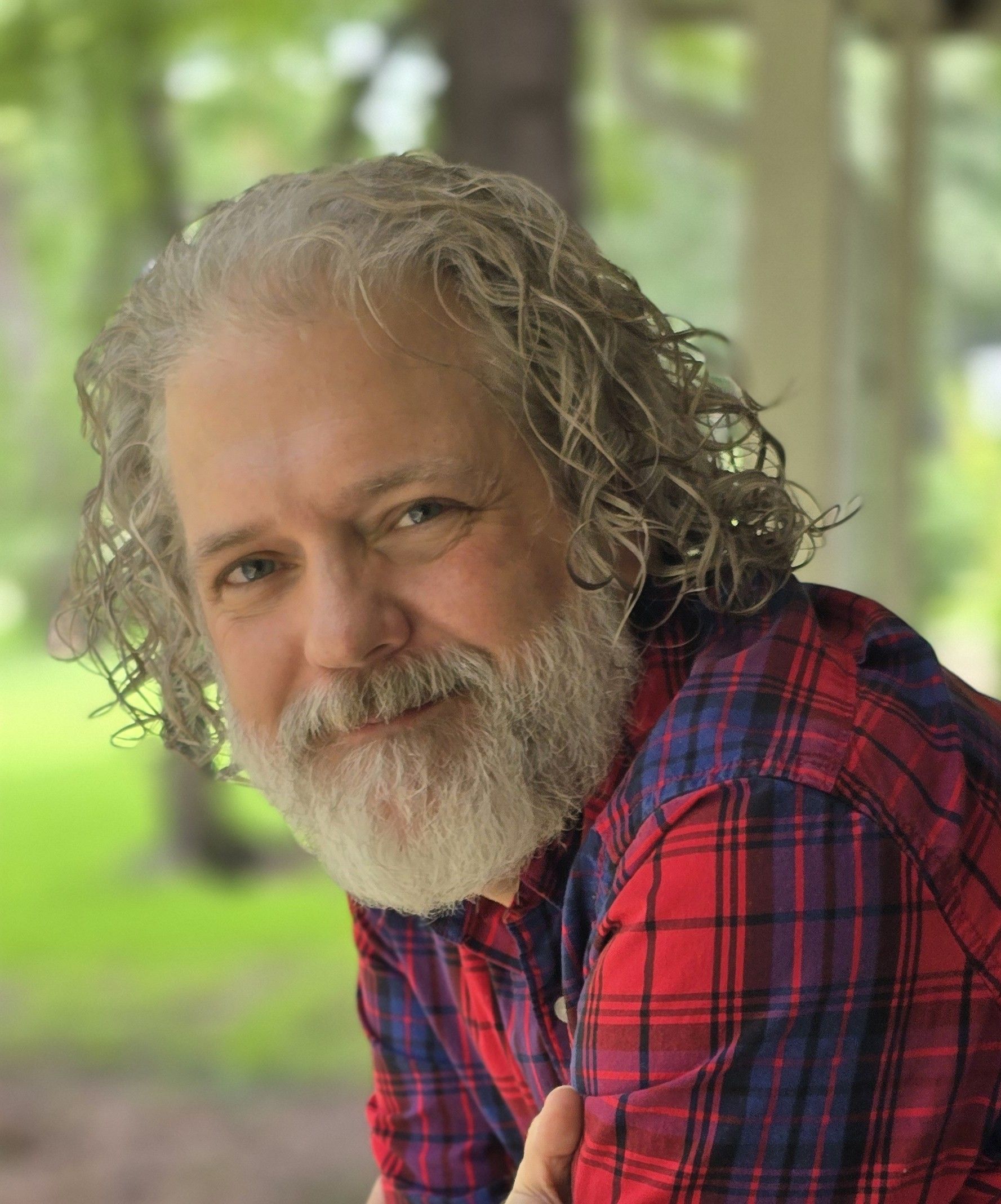 Person with gray curly hair in a red and blue shirt smiles