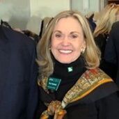 Woman with blonde hair wearing a black turtleneck, printed scarf, and smiling.
