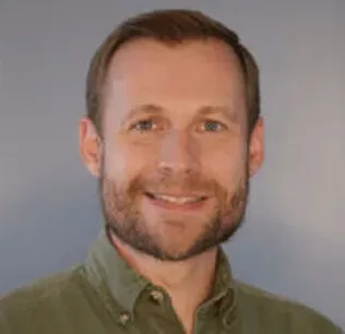 Man with a short beard smiles, wearing a green button-down shirt.