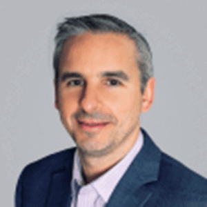 Man in blue blazer and open-collared shirt, smiling, headshot with neutral background.