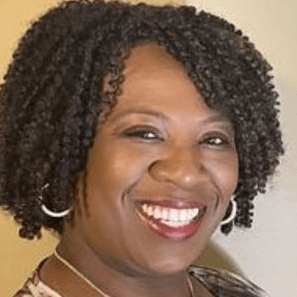 Smiling woman with curly black hair, wearing silver hoop earrings.
