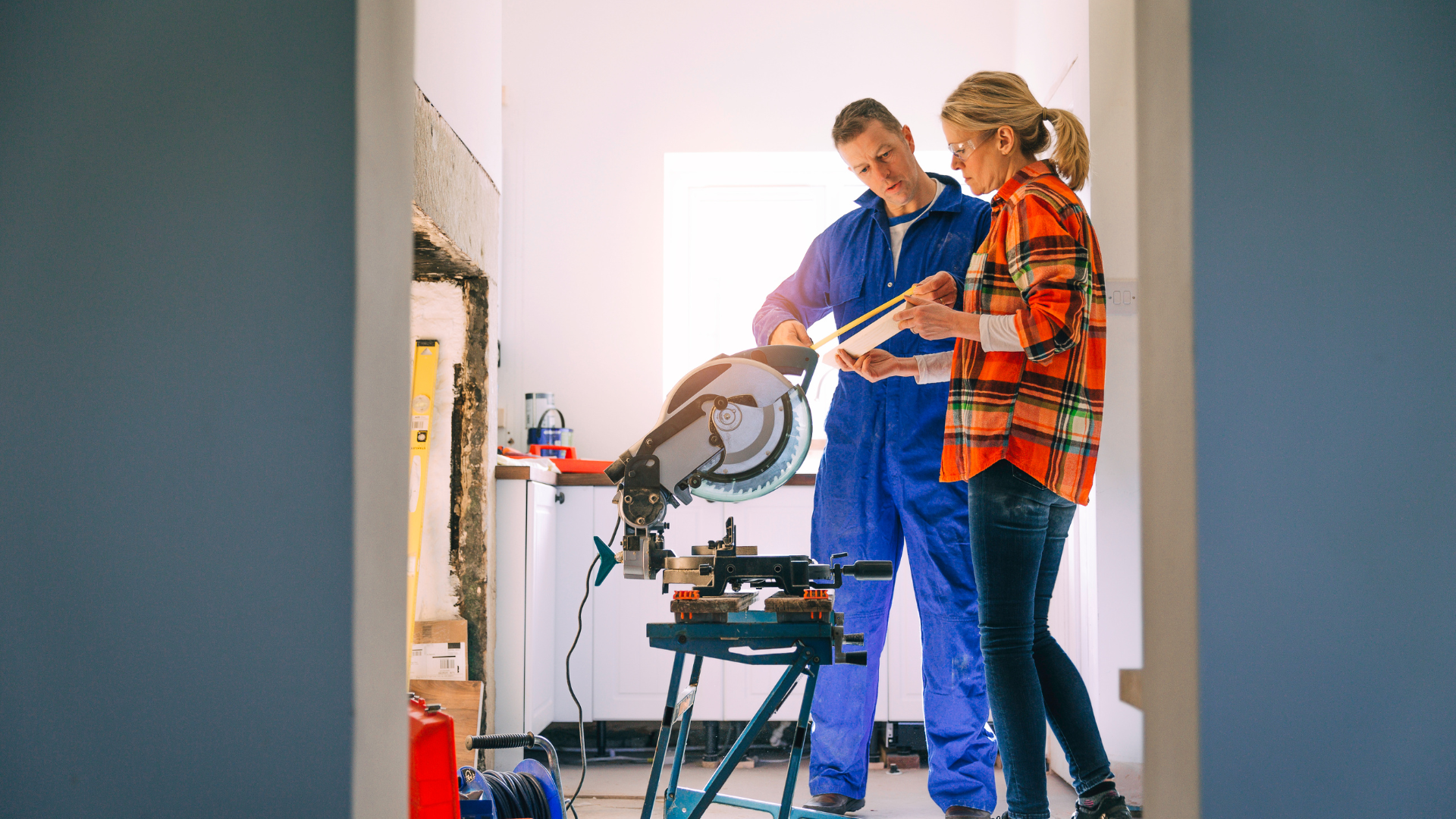 A man and a woman are standing next to a circular saw in a room.