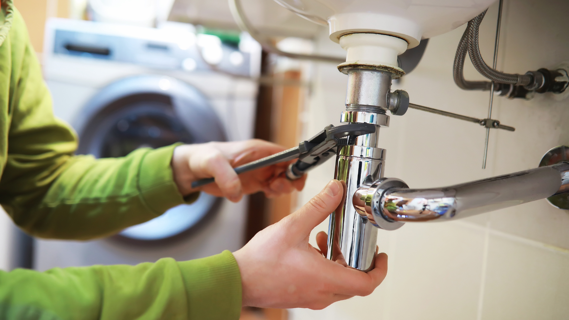 A plumber is fixing a sink with a wrench.