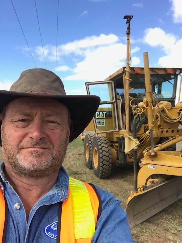 A man wearing a cowboy hat is standing in front of a cat tractor.