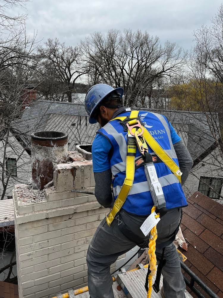 A guardian chimney solutions technician wearing a hard hat and safety vest is working on a chimney on top of a roof.