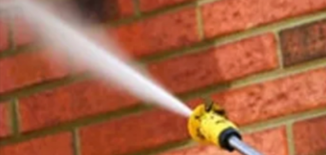 A person is using a high pressure washer to clean a brick wall.